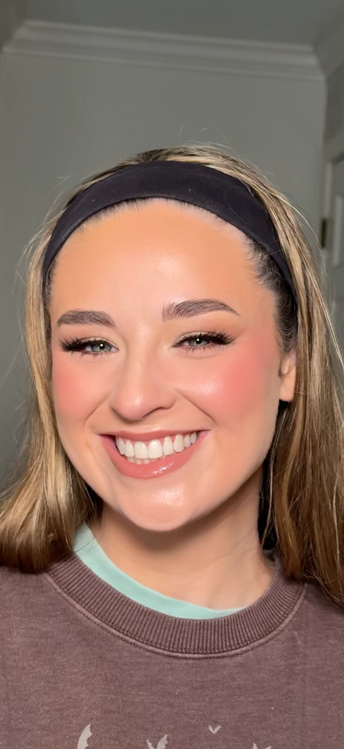 Close-up of a smiling woman wearing a black headband and a brown sweatshirt indoors.
