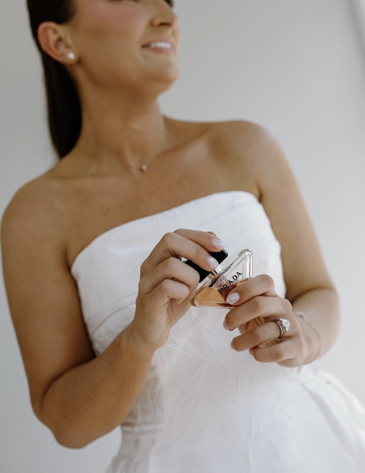 A woman in a white strapless dress holding a Prada perfume bottle.