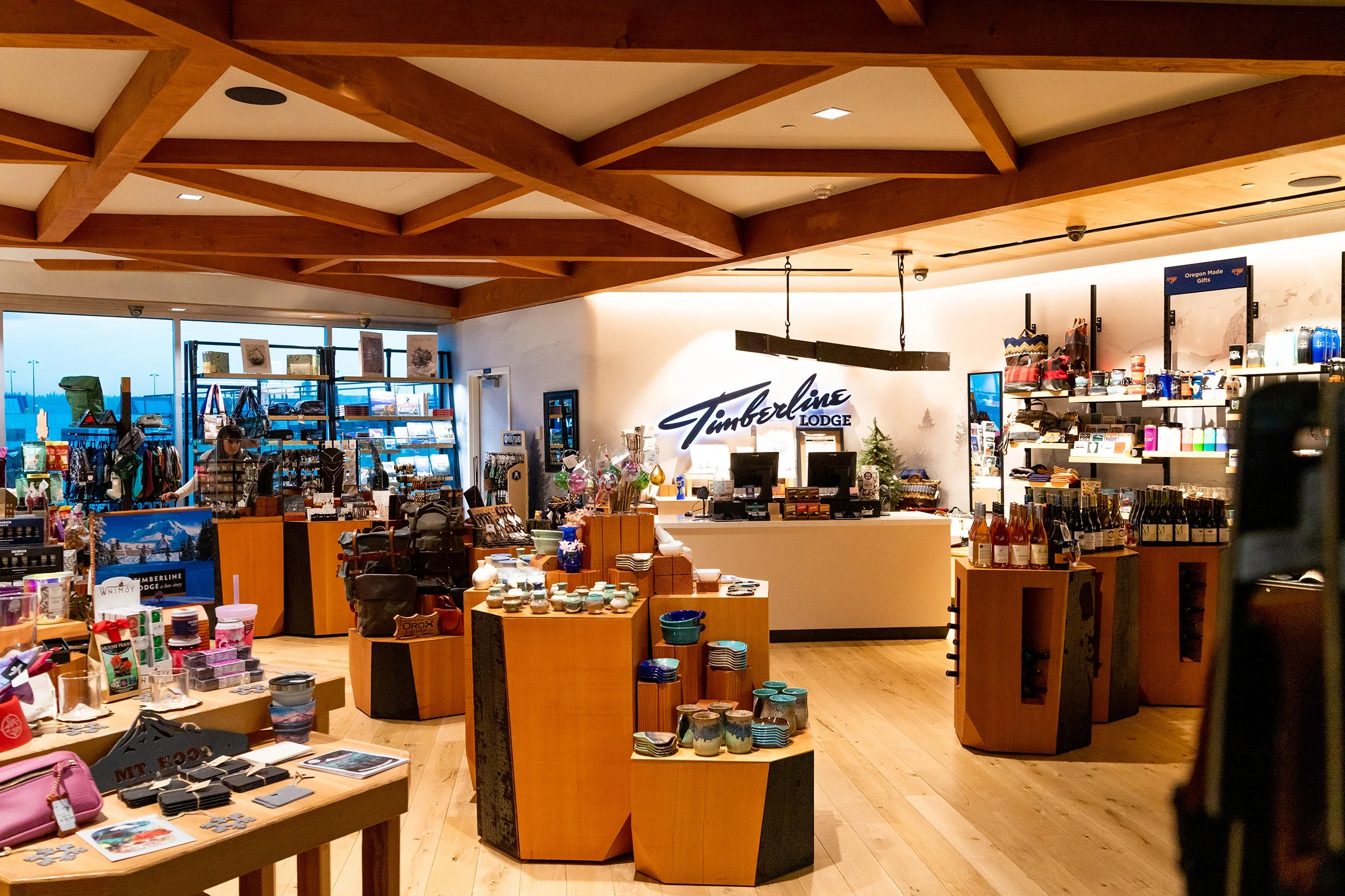 Inside Timberline Lodge gift shop displaying various souvenirs, apparel, and decorative items with a lit sign that says Timberline Lodge behind the counter.