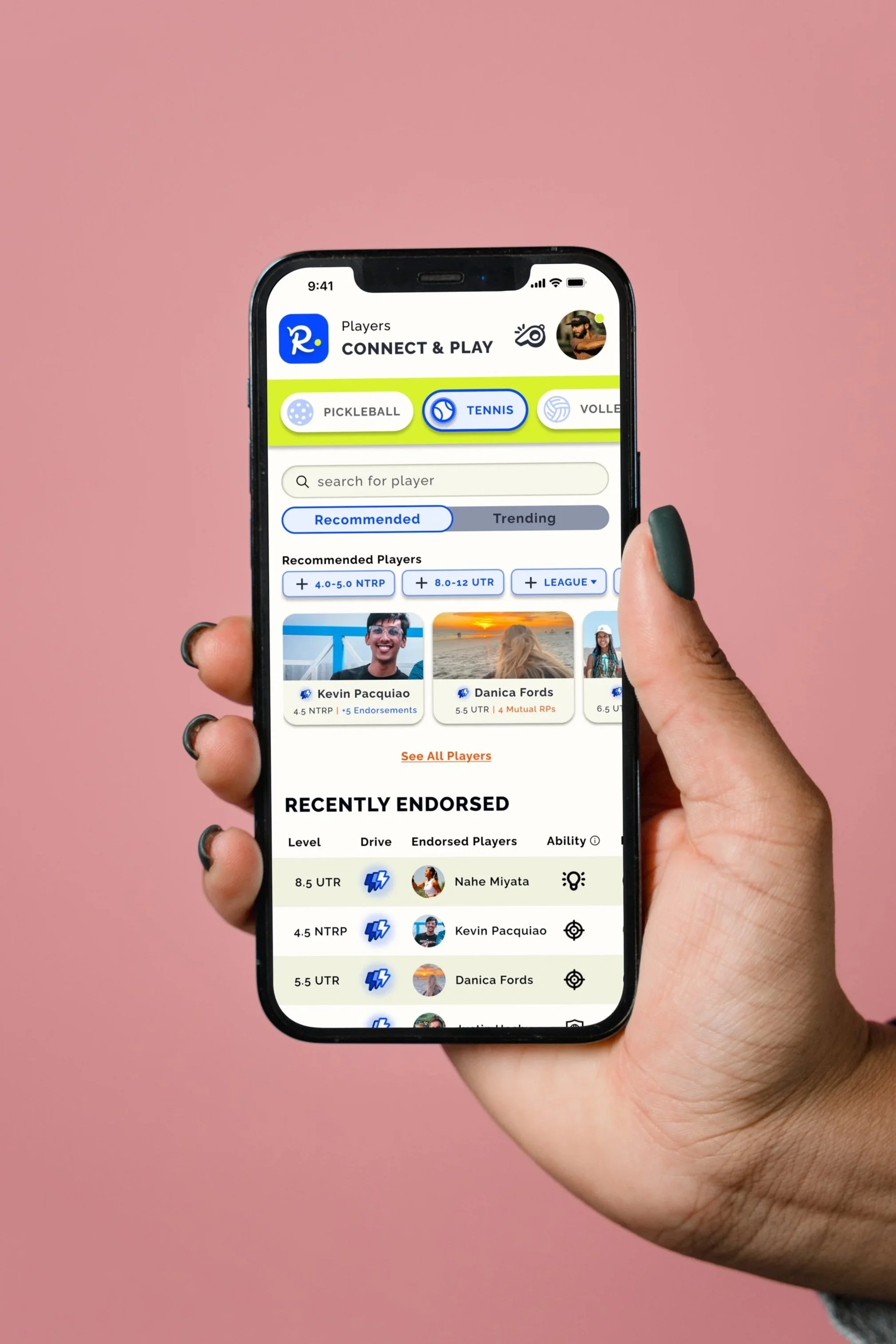 A person holding a smartphone displaying a tennis players app with recommended and recently endorsed players on a pink background.