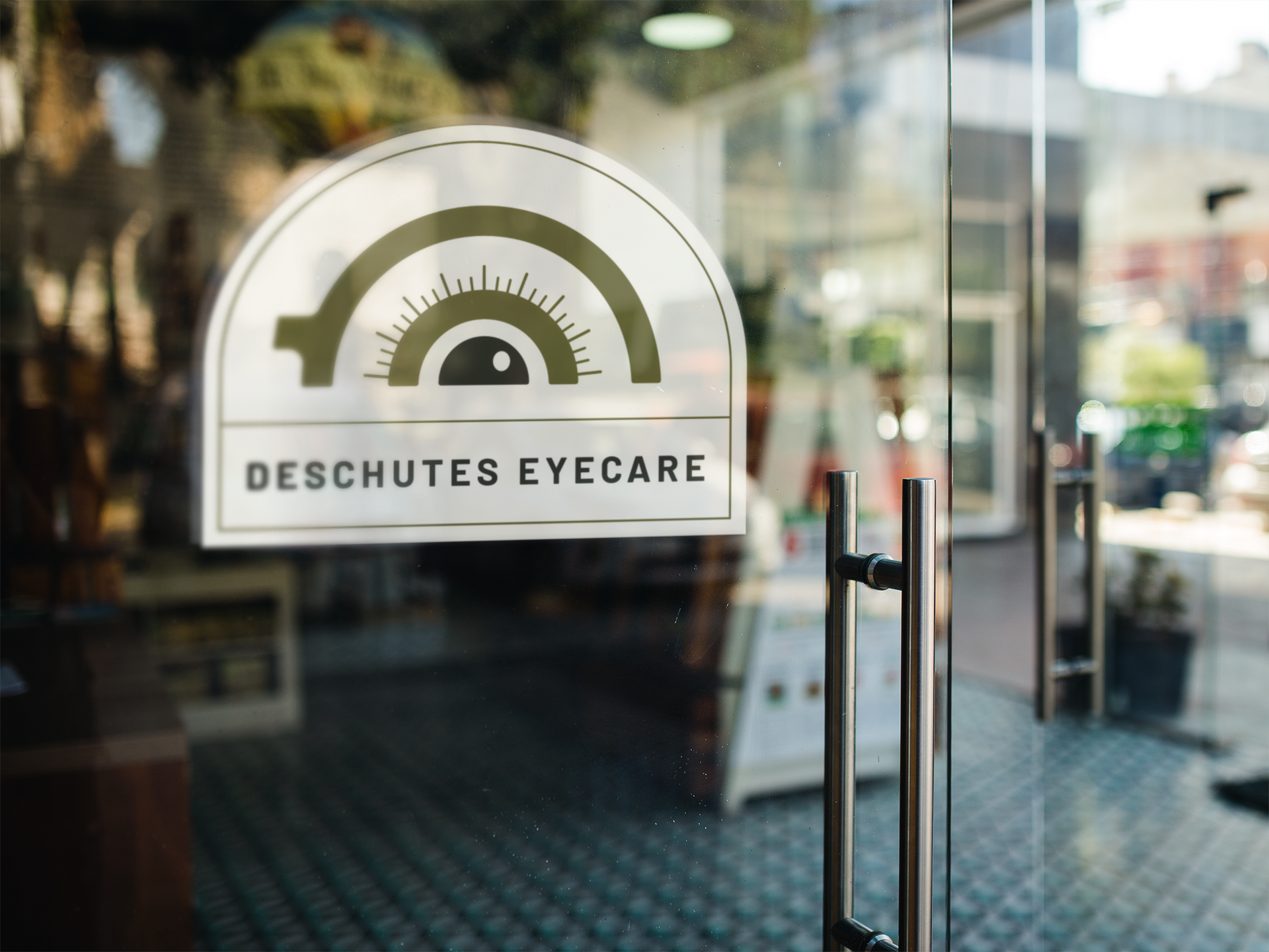 Glass door with a decal sign for Deschutes Eyecare, featuring a stylized eye chart graphic with a semi-circle and lines, and black text.