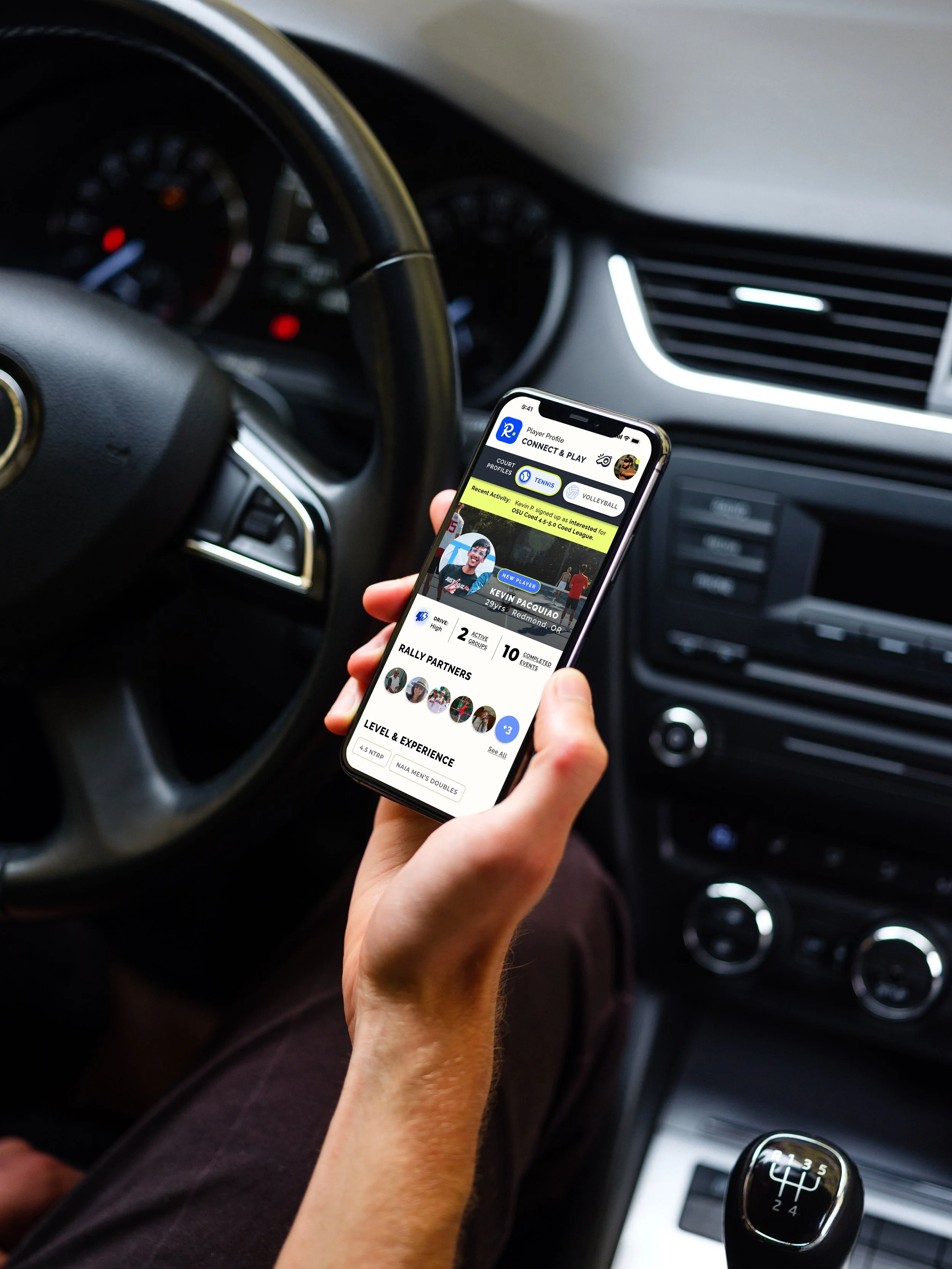 Person holding a smartphone displaying a sports team app inside a car with a manual gear shift.