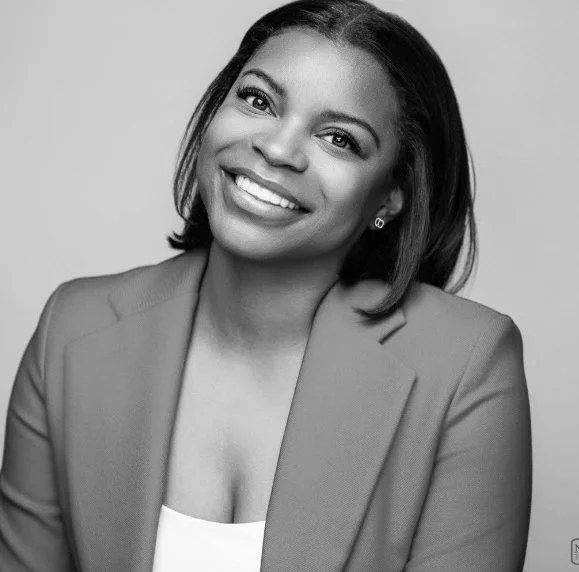 Black and white portrait of a smiling woman with shoulder-length hair wearing a blazer and a white top.