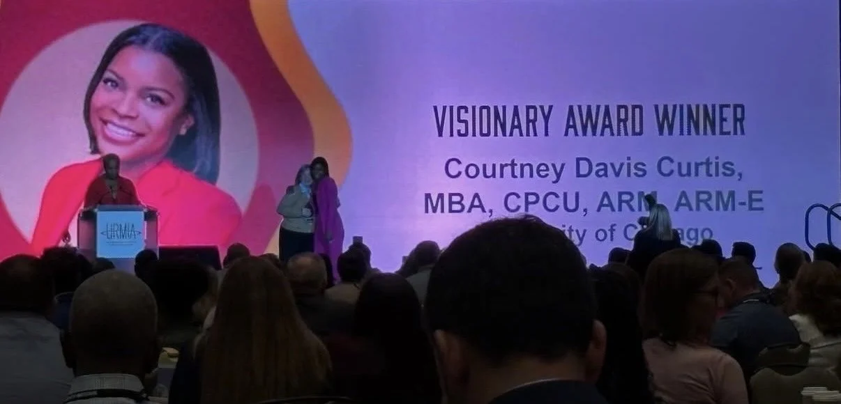 A woman on stage receiving an award at a conference, with a large screen behind her displaying her name, credentials, and photo, recognizing her as a visionary award winner.