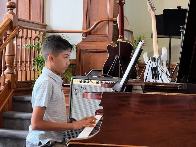 A boy reading sheet music while performing on a grand piano during Lifelong Music School's annual recital.