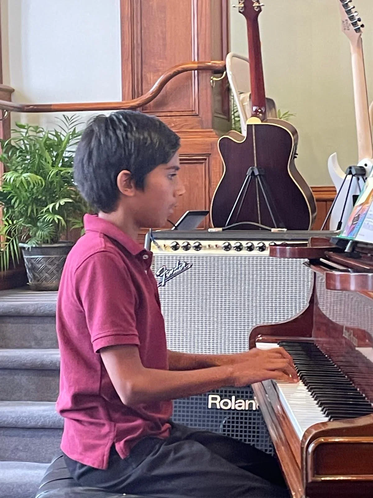 A boy reading sheet music while performing on a grand piano during Lifelong Music School's annual recital.
