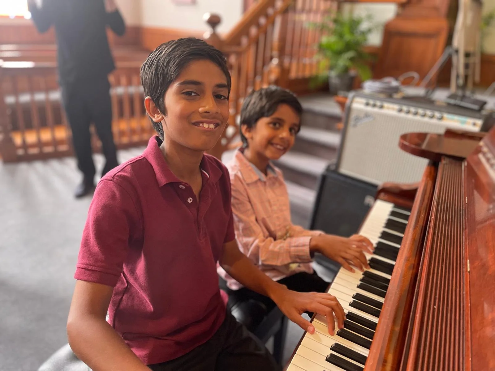 Two brothers sitting at a grand piano after Lifelong Music School's 2024 annual recital. They are smiling as they press the piano keys.