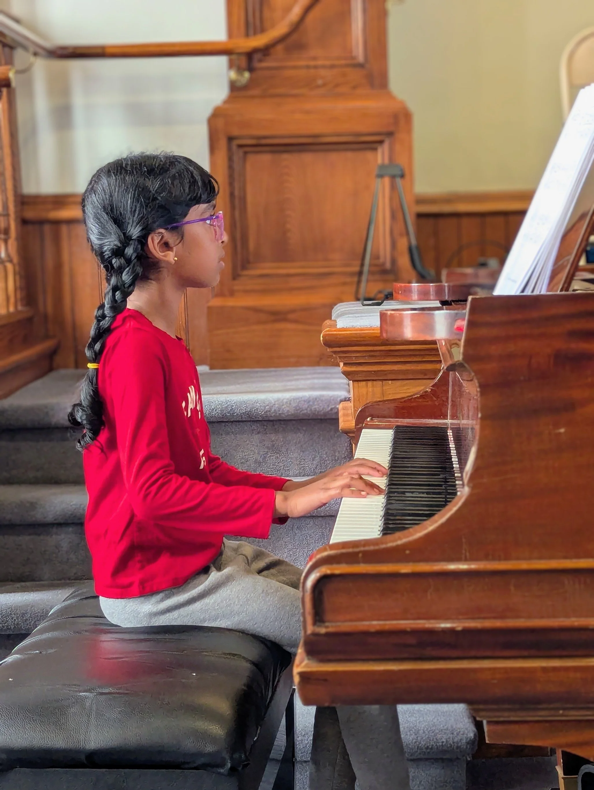 A young girl reading sheet music while performing on a grand piano during Lifelong Music School's 2025 annual recital in Hunterdon County, NJ.