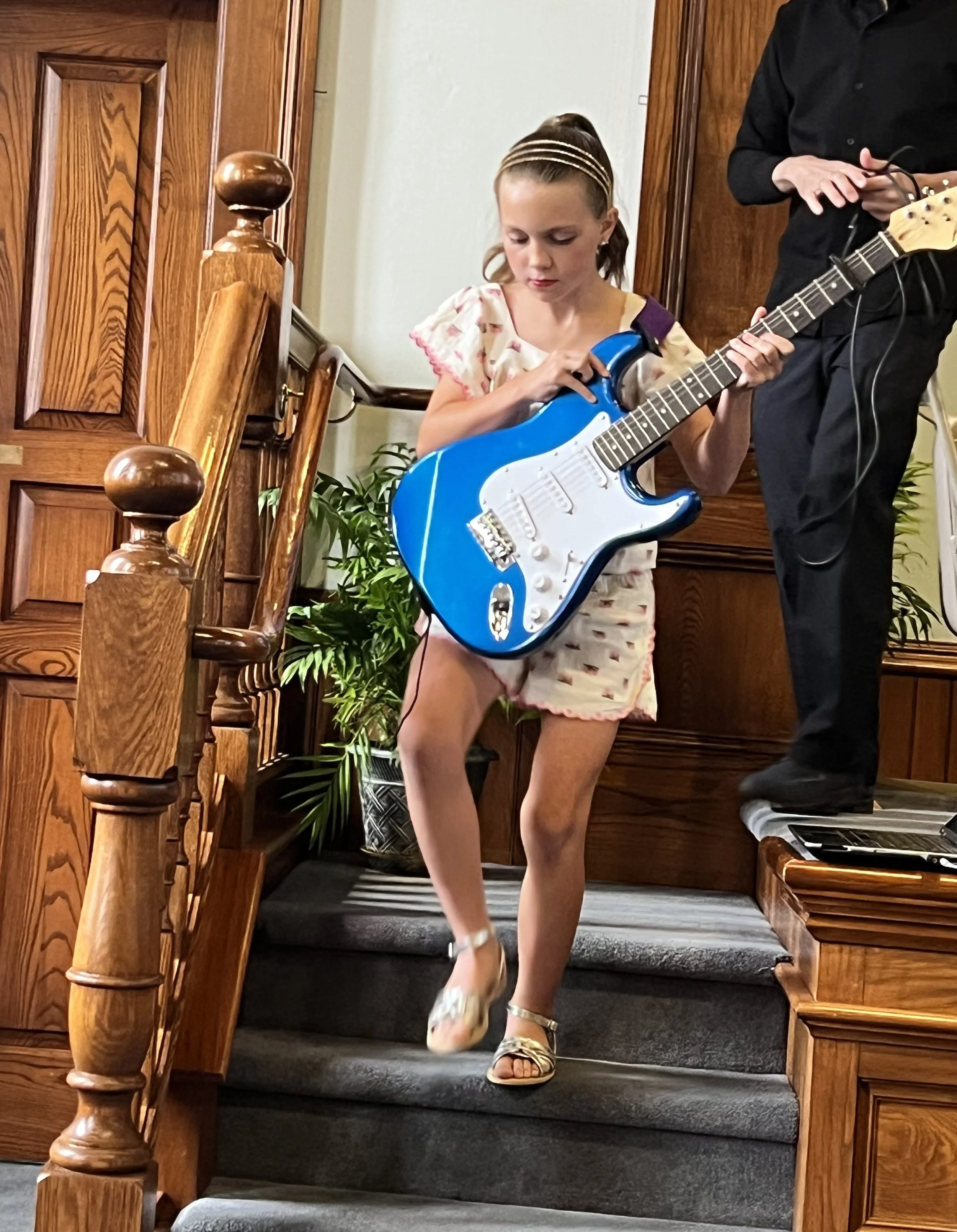A girl walking off stage while carrying an electric guitar after her performance at Lifelong Music School's 2024 annual recital.