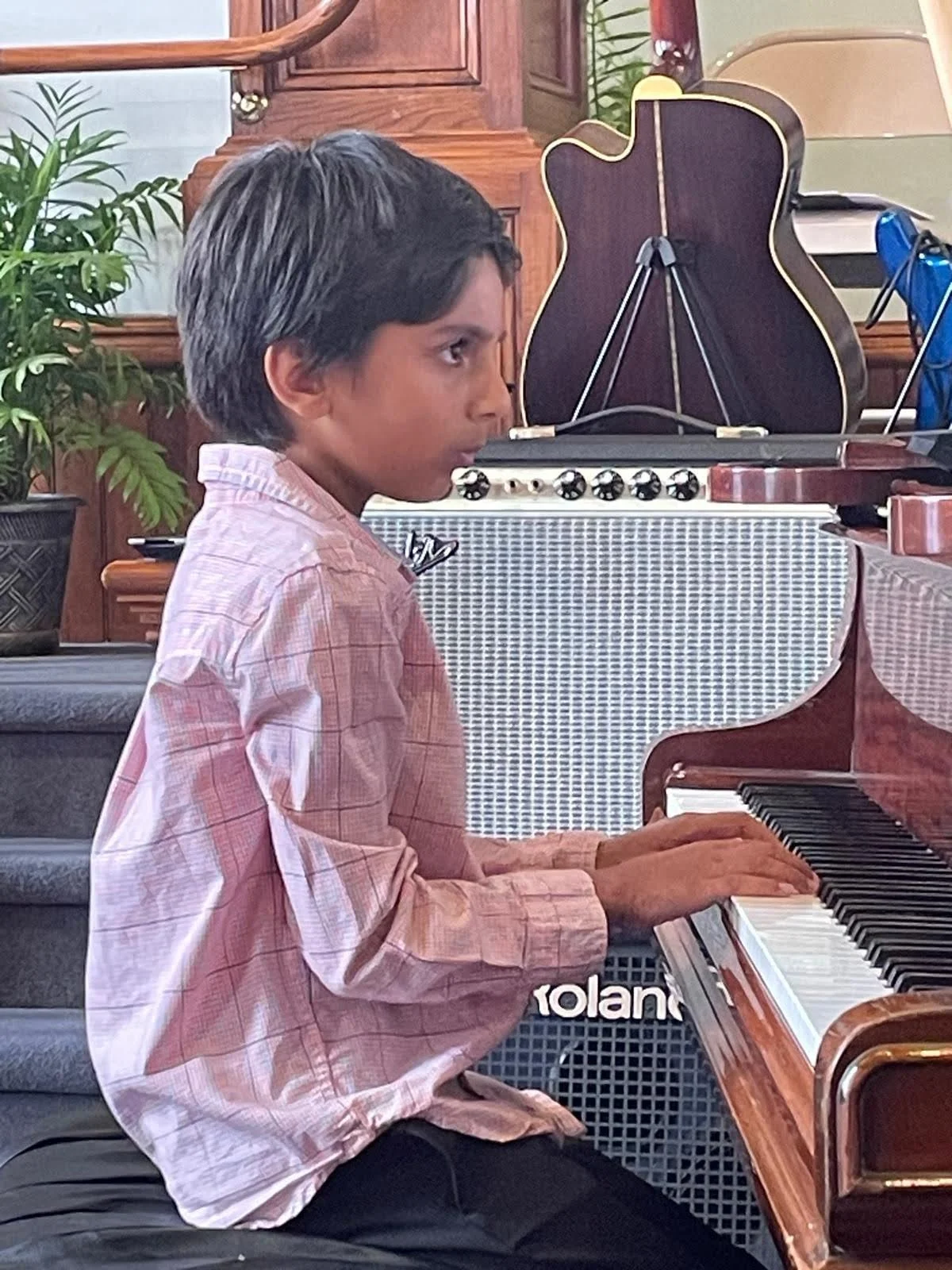 A boy reading sheet music while performing on a grand piano during Lifelong Music School's annual recital.