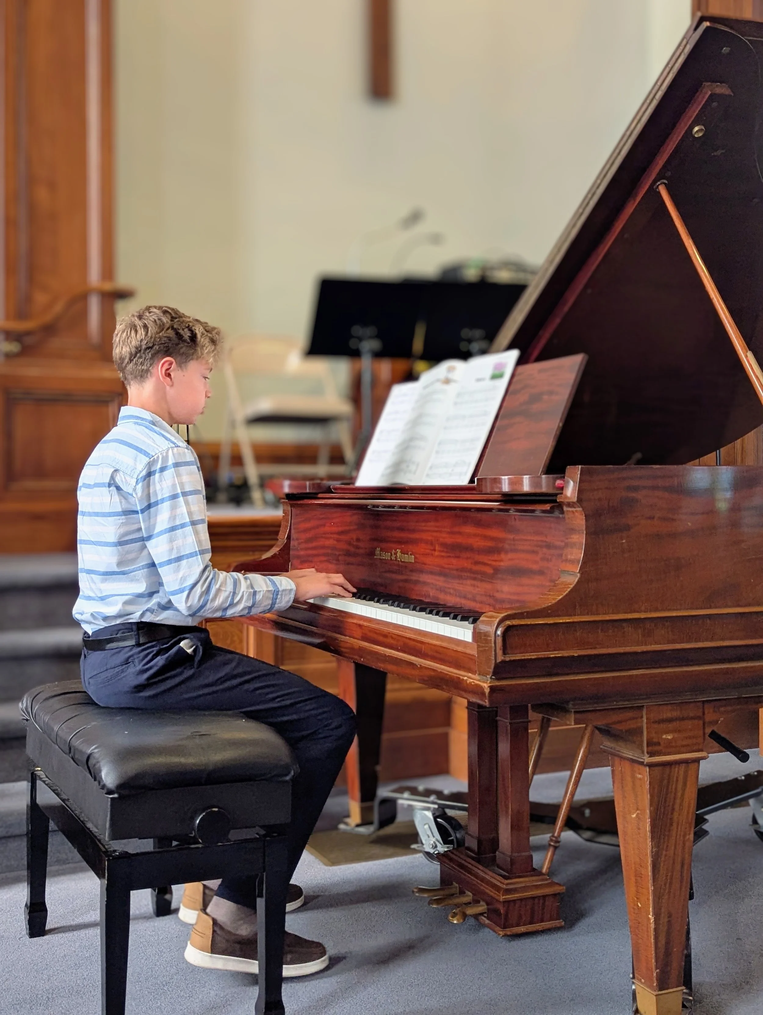 A boy reading sheet music while performing on a grand piano during Lifelong Music School's 2025 annual recital in Hunterdon County, NJ.