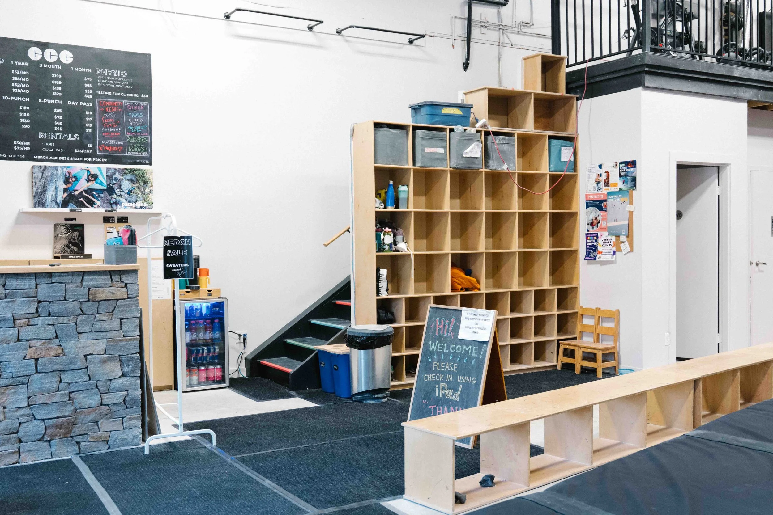 Interior of a climbing gym with a black hanging bar, wooden cubby shelves, a wooden bench, and a 