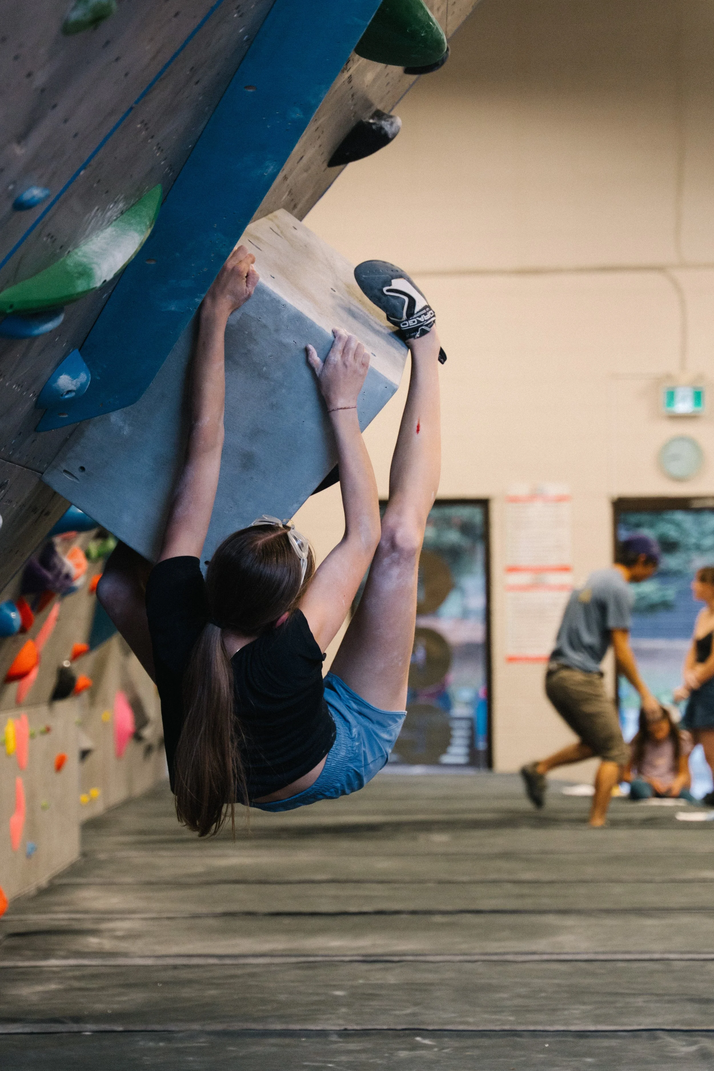 A young girl is climbing a rock wall at an indoor climbing gym.