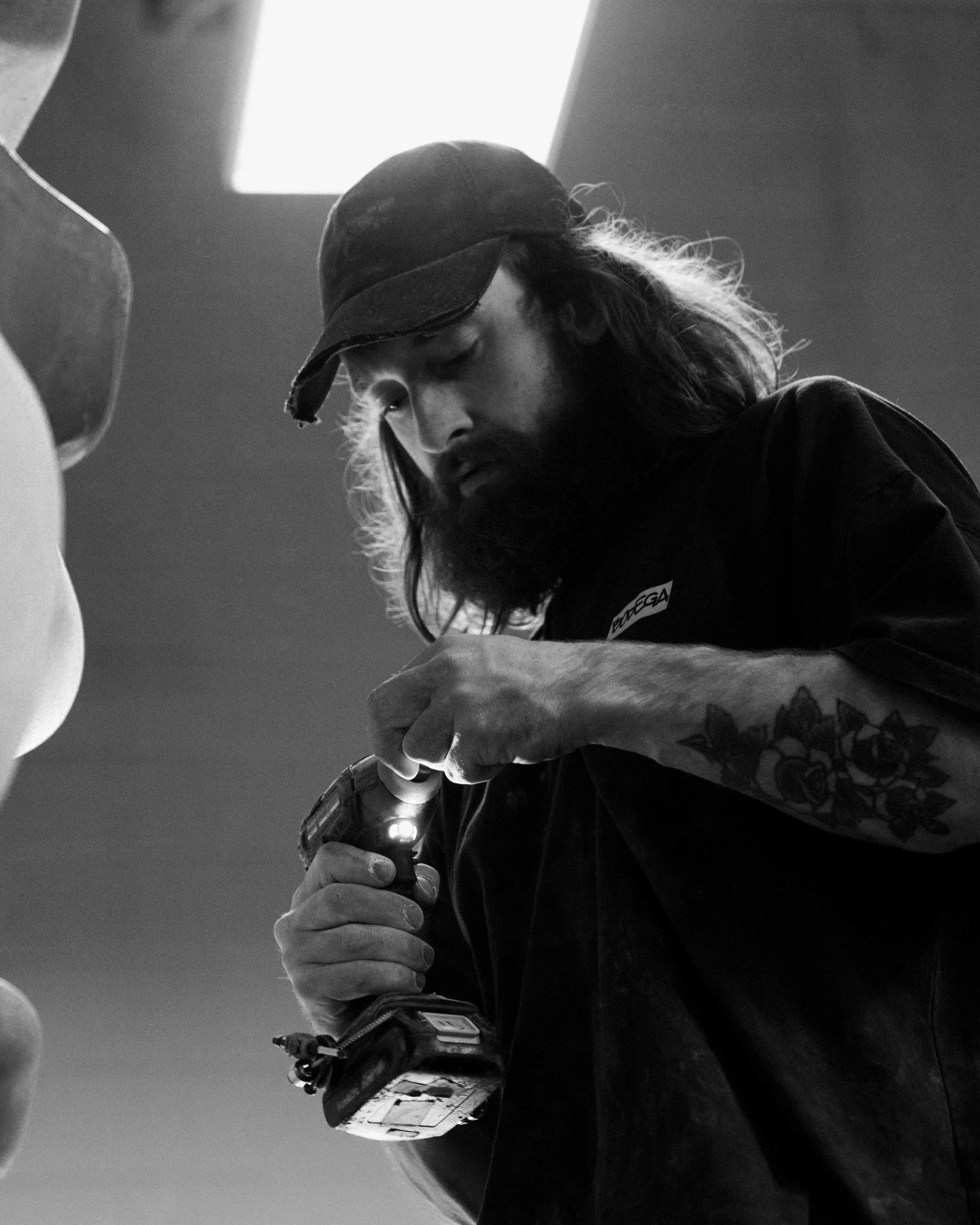 Black and white photo of a man wearing a cap and Gloves holding a power drill.
