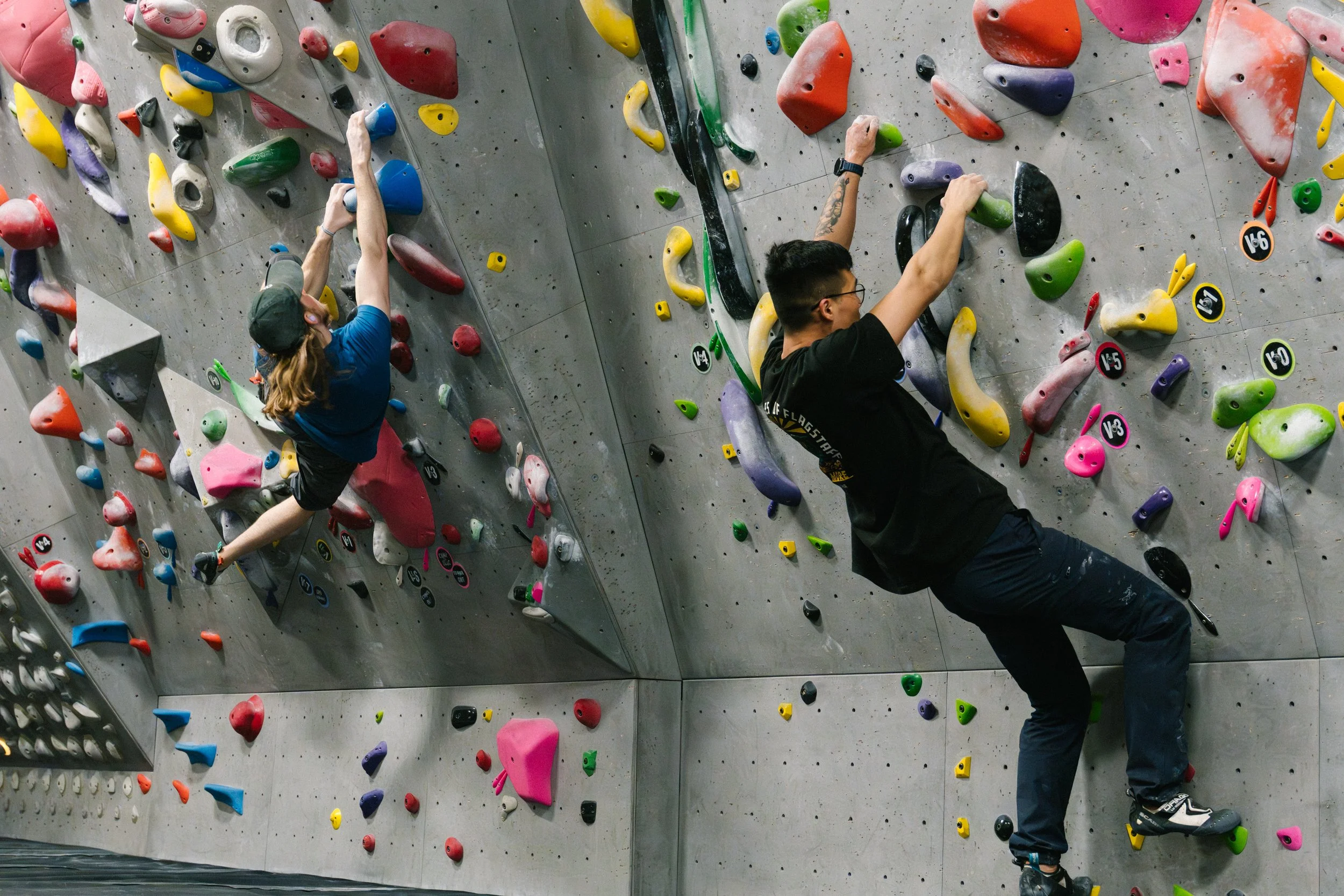 Two people climbing an indoor rock wall with colorful holds.
