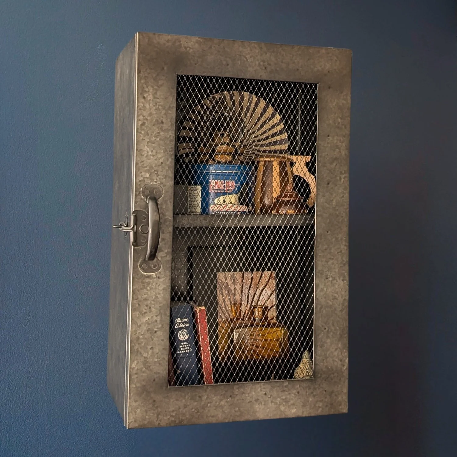 Vintage metal wall cabinet with wire mesh door styled with books and decor in an industrial teen bedroom designed by Caroline by Design in Montclair, NJ.