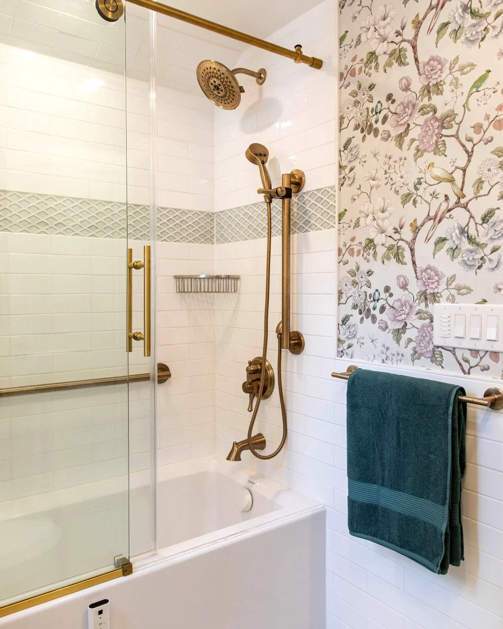 Shower and tub with brass fixtures, subway tile, and floral wallpaper in botanical primary bathroom by Caroline by Design.
