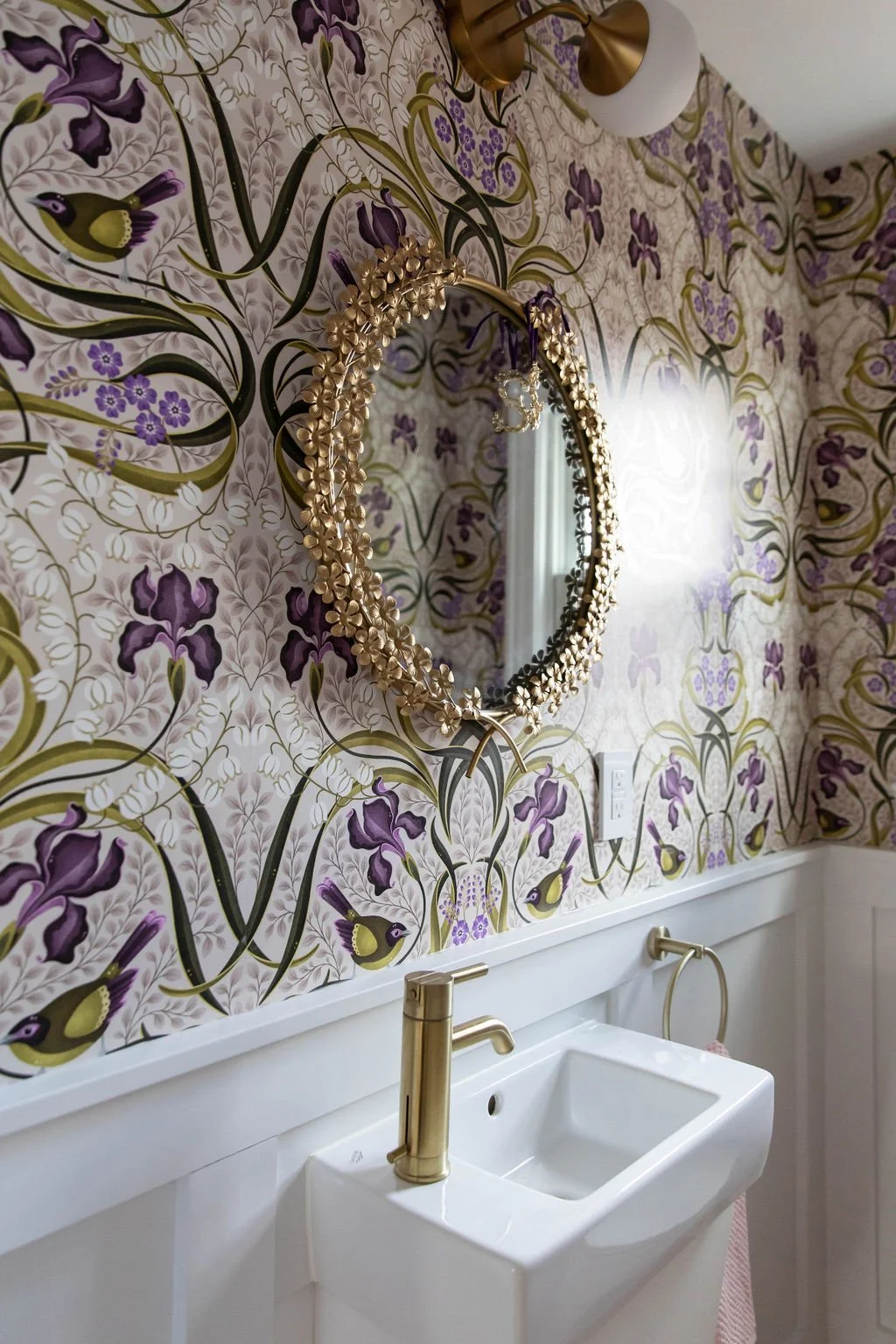 Powder room vanity with botanical wallpaper, brass faucet, and decorative mirror.