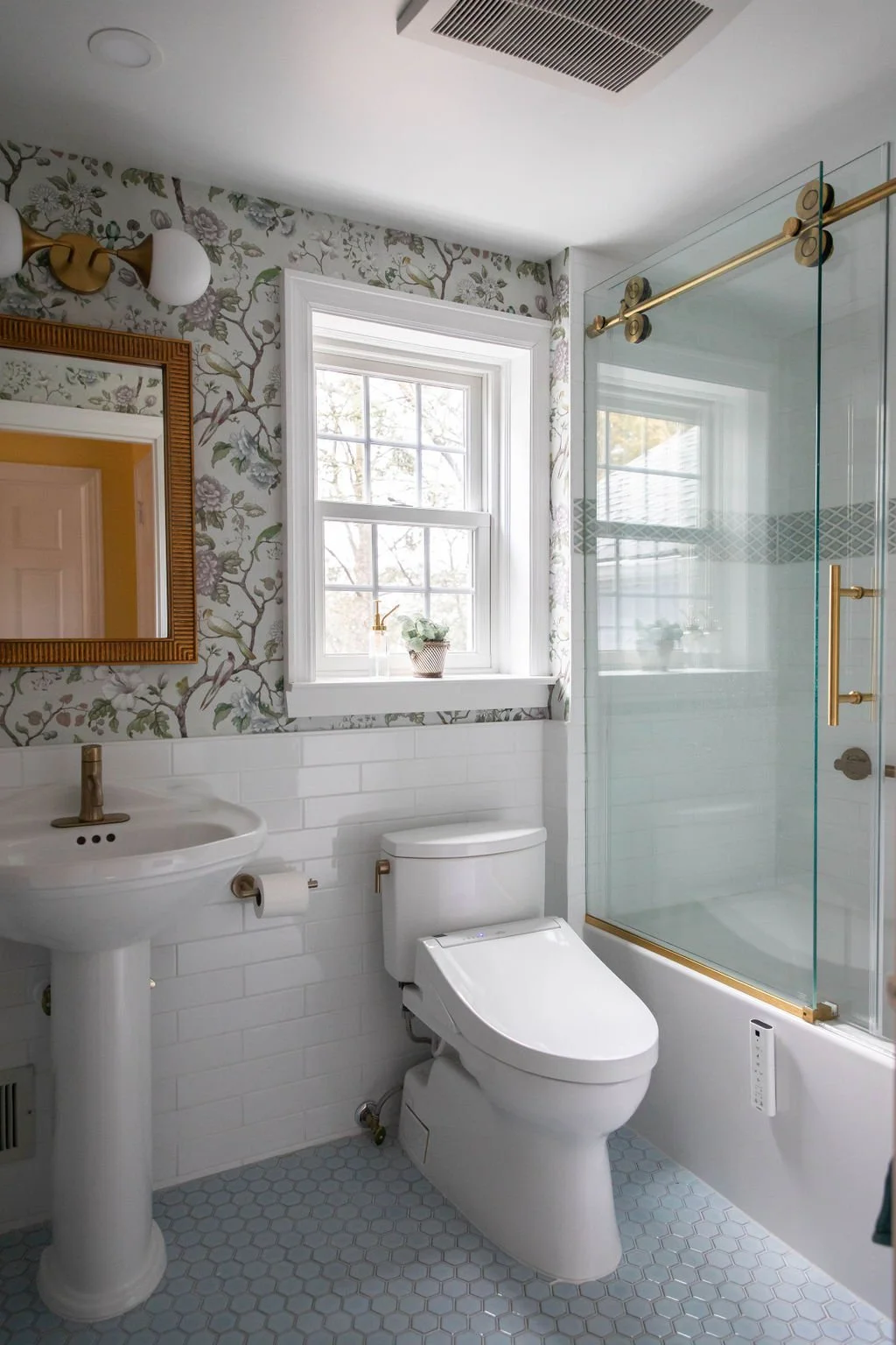 Montclair NJ primary bathroom by Caroline by Design showing hexagon mosaic floor tile, white subway tile walls, brass hardware, and floral wallpaper with birds and peonies creating a tailored historic-home look suited for daily living.