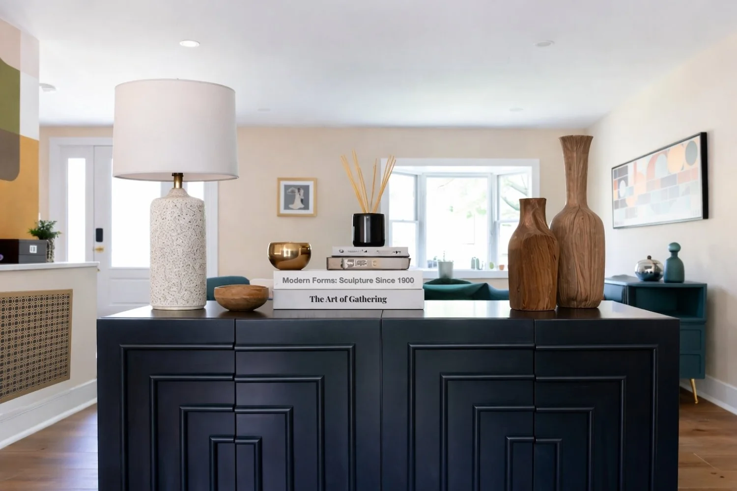Eclectic living room sideboard styling with stacked design books, carved wood vases, and ceramic lamp in Montclair, NJ designed by Caroline by Design.