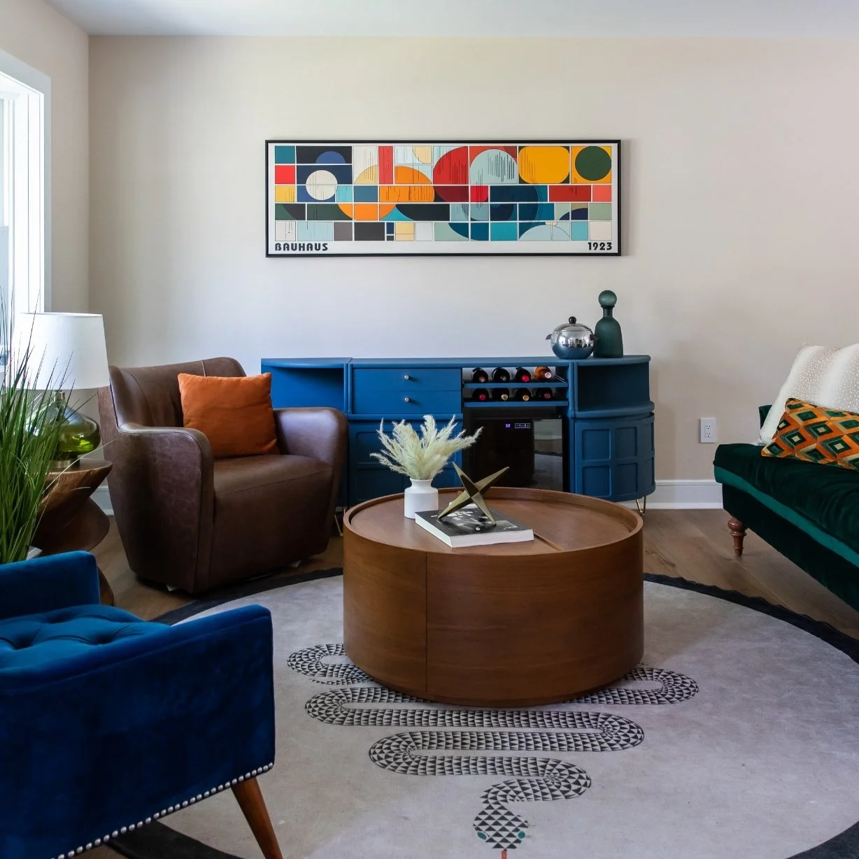 Collected open concept living room by Caroline by Design featuring jewel-tone seating, Bauhaus artwork, a round wood coffee table, and a sculptural rug in a Montclair NJ home.