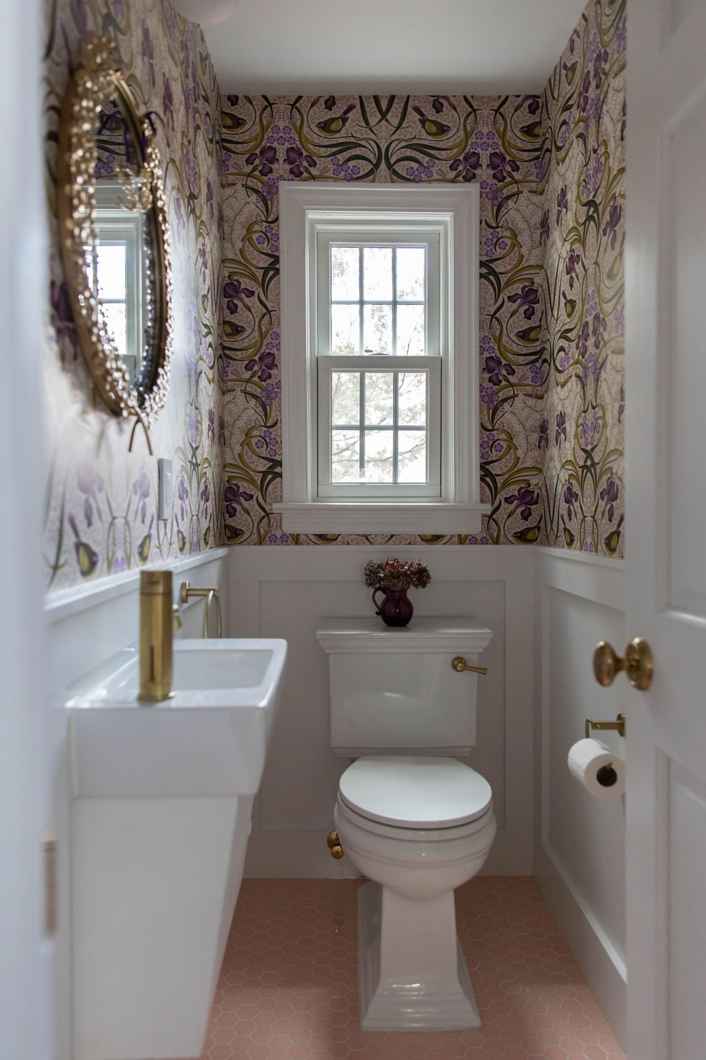 A small space with big personality. This powder room pairs bold botanical wallpaper with soft blush tile, sculptural brass details, and classic millwork for a space that feels playful, layered, and timeless.