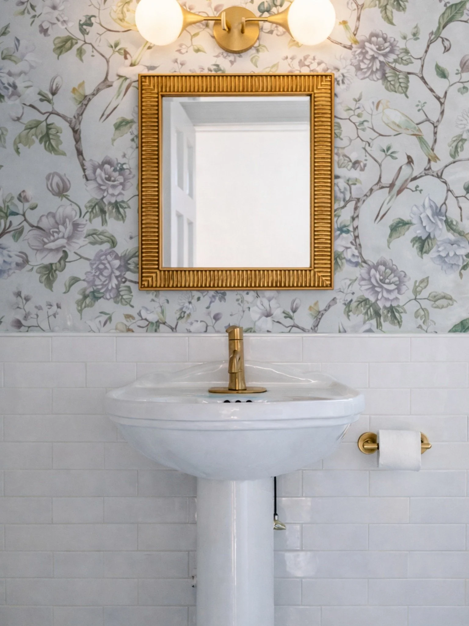 Pedestal sink with floral wallpaper and brass mirrors in botanical primary bathroom designed by Caroline by Design.