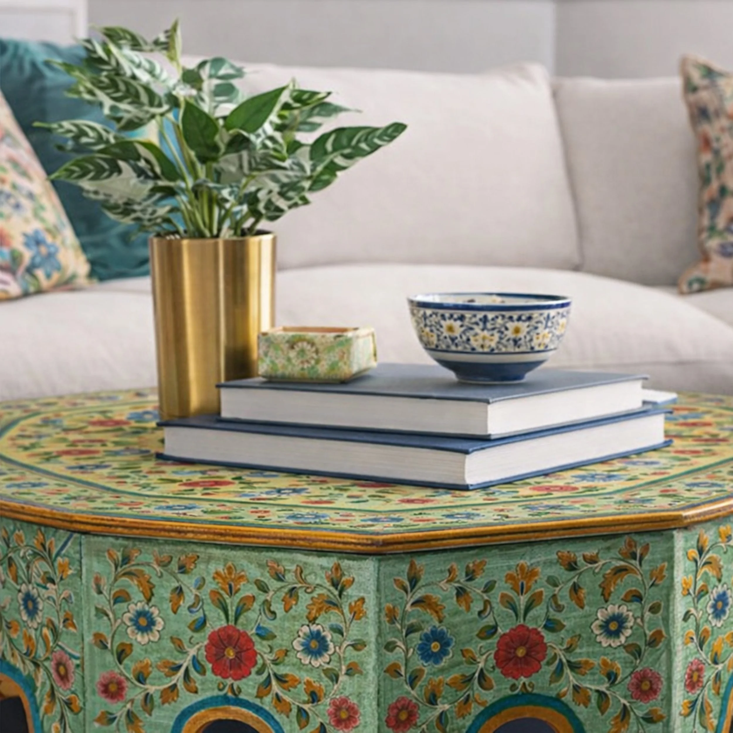 Close-up of green hand-painted floral coffee table styled with books and brass planter in eclectic living room by Caroline By Design, Montclair NJ