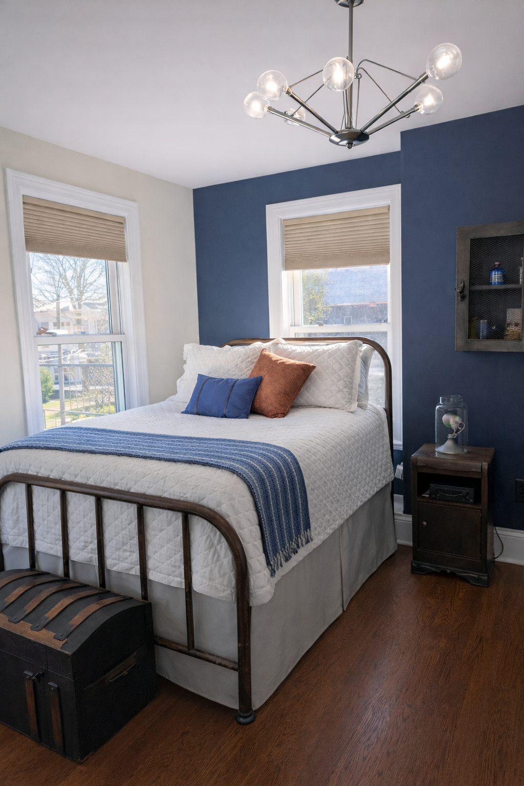 Vintage industrial teen bedroom featuring a metal bed frame, navy accent wall, neutral bedding, and modern chandelier, designed by Caroline by Design in Montclair, New Jersey.