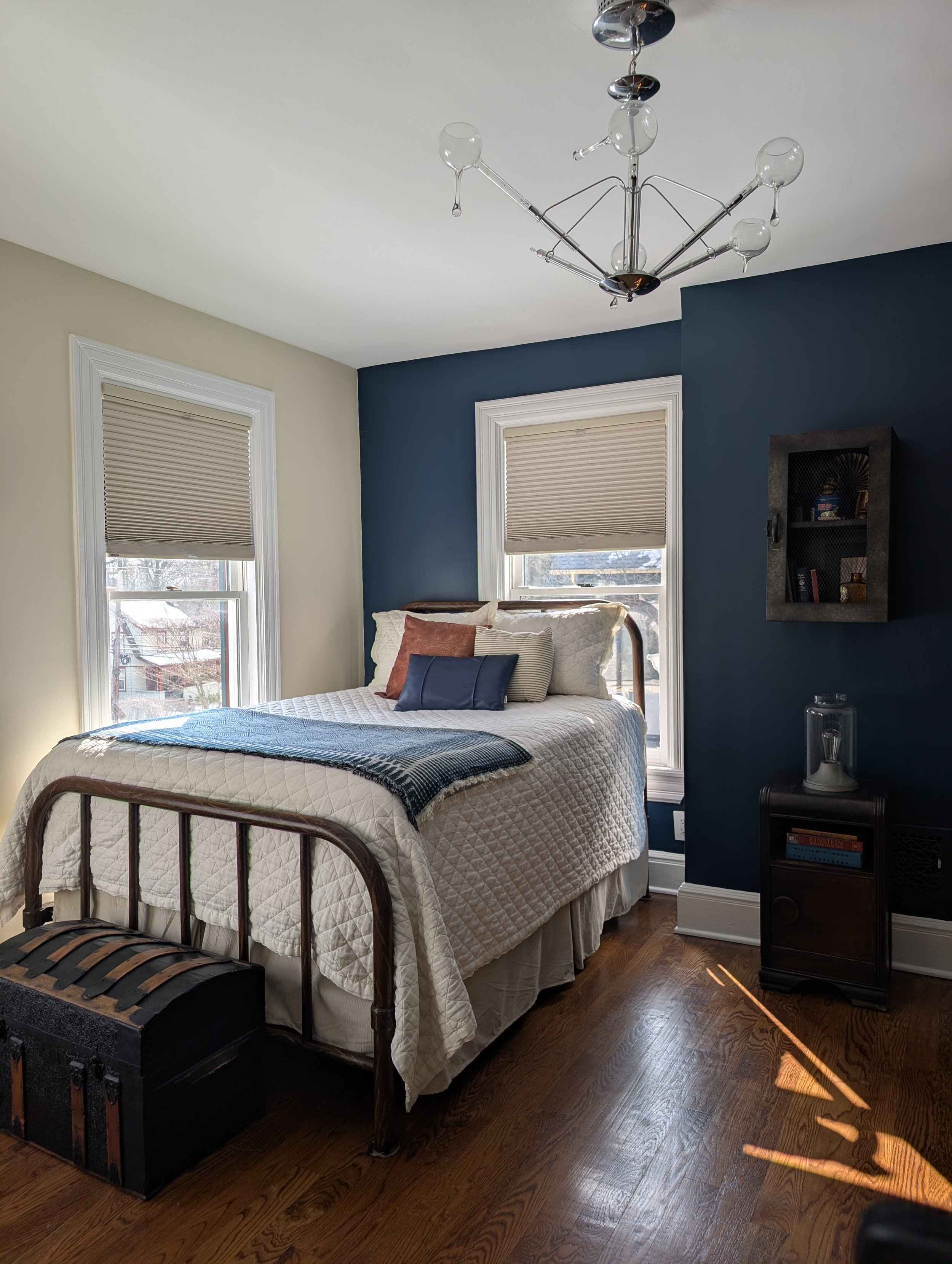 Vintage industrial teen bedroom featuring a metal bed frame, navy accent wall, neutral bedding, and modern chandelier, designed by Caroline by Design in Montclair, New Jersey.