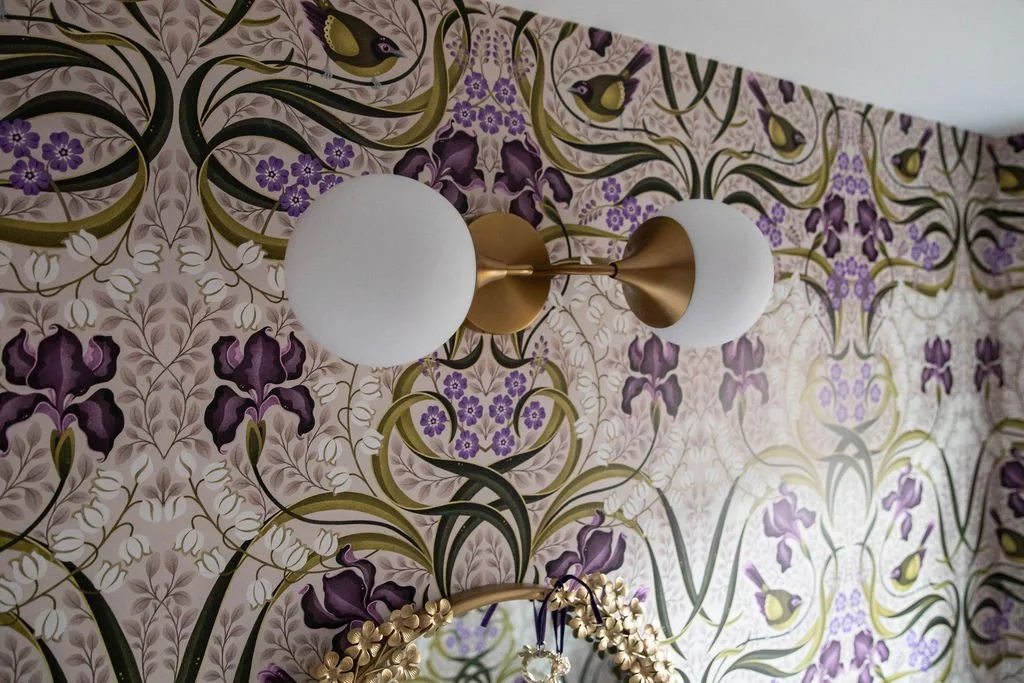 Brass globe sconce mounted on botanical wallpaper in a colorful powder bathroom.