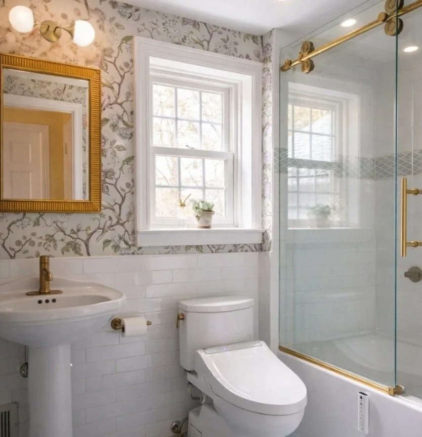 Primary bathroom designed by Caroline by Design featuring floral wallpaper, brass shower fixtures, subway tile, and hexagon floor tile.
