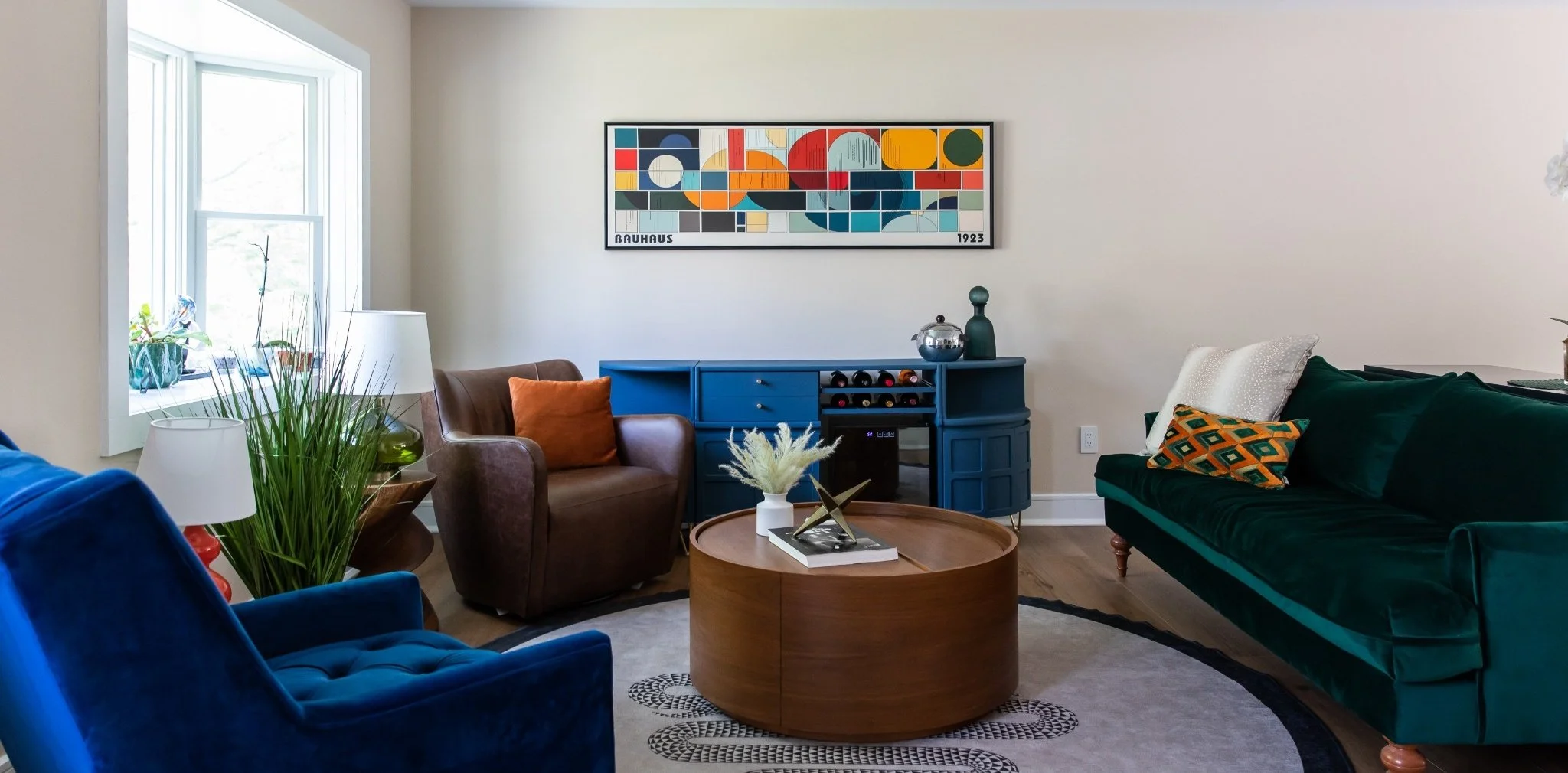 Collected open concept living room by Caroline by Design featuring jewel-tone seating, Bauhaus artwork, a round wood coffee table, and a sculptural rug in a Montclair NJ home.