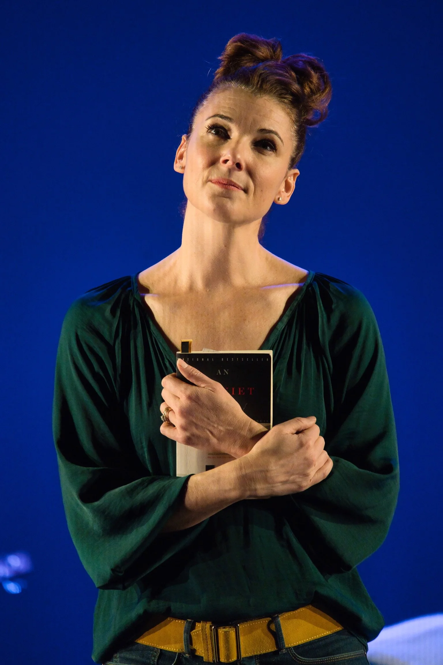 Chryssie Whitehead on stage for In My Own Little Corner holding a book close to her chest, standing against a dark blue background.