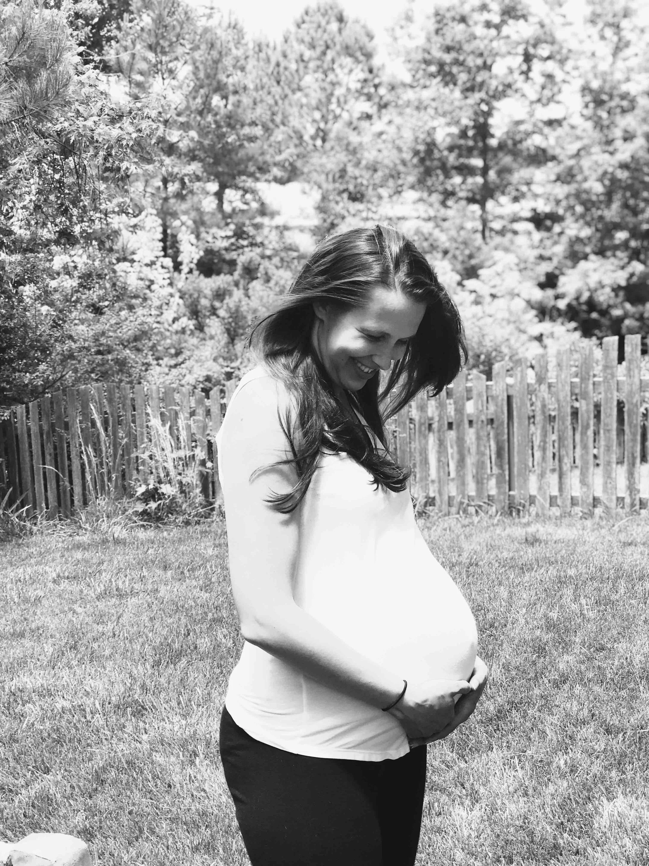 Pregnant woman smiling and holding belly outside