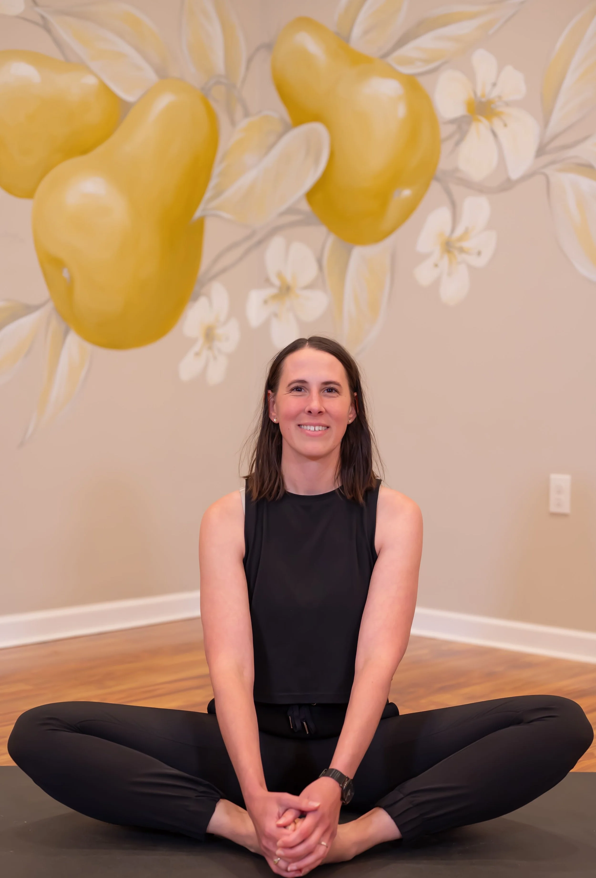 Woman sitting on mat doing yoga with a pear mural behind her