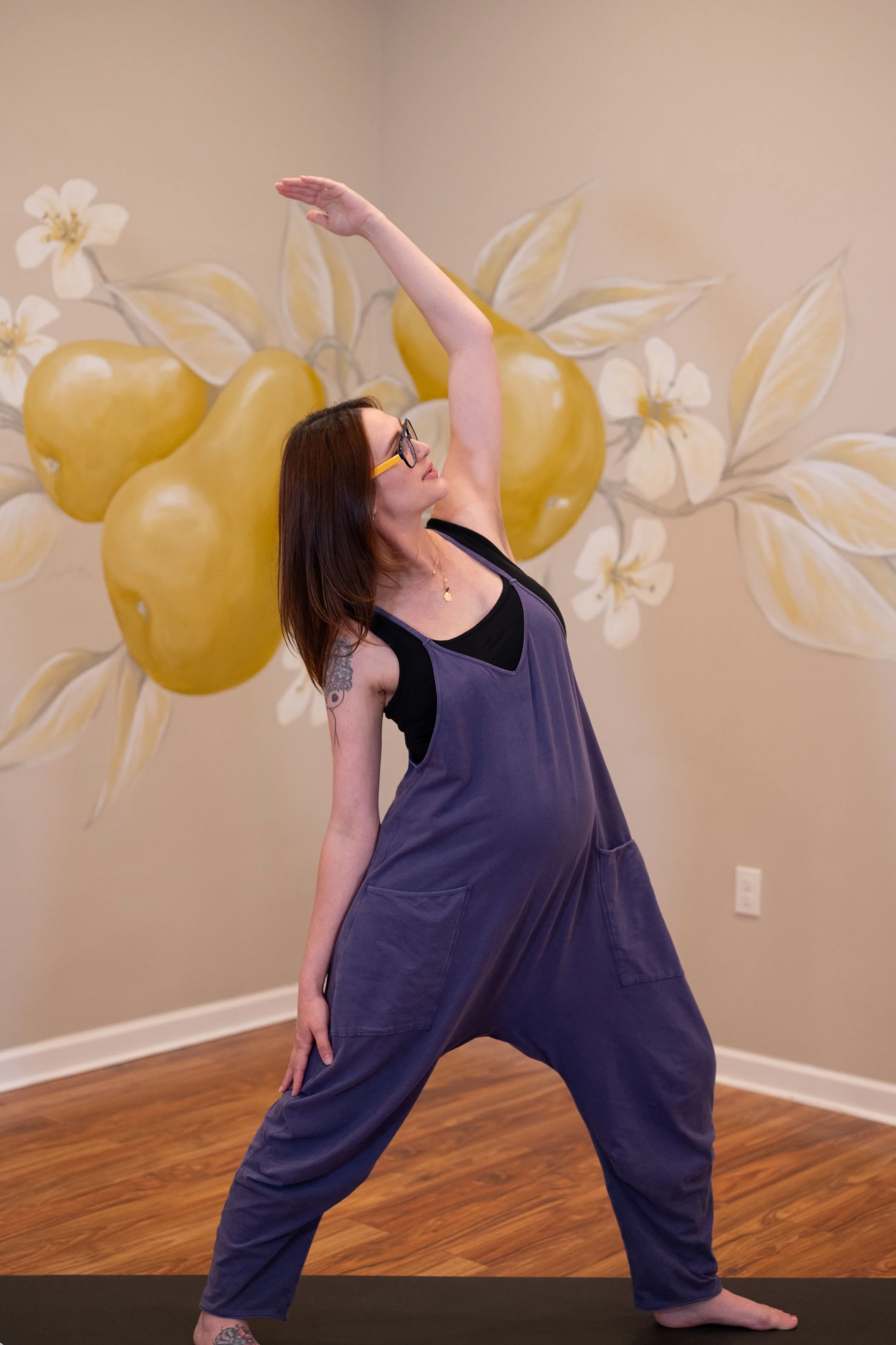 A pregnant woman doing yoga with pear mural behind her