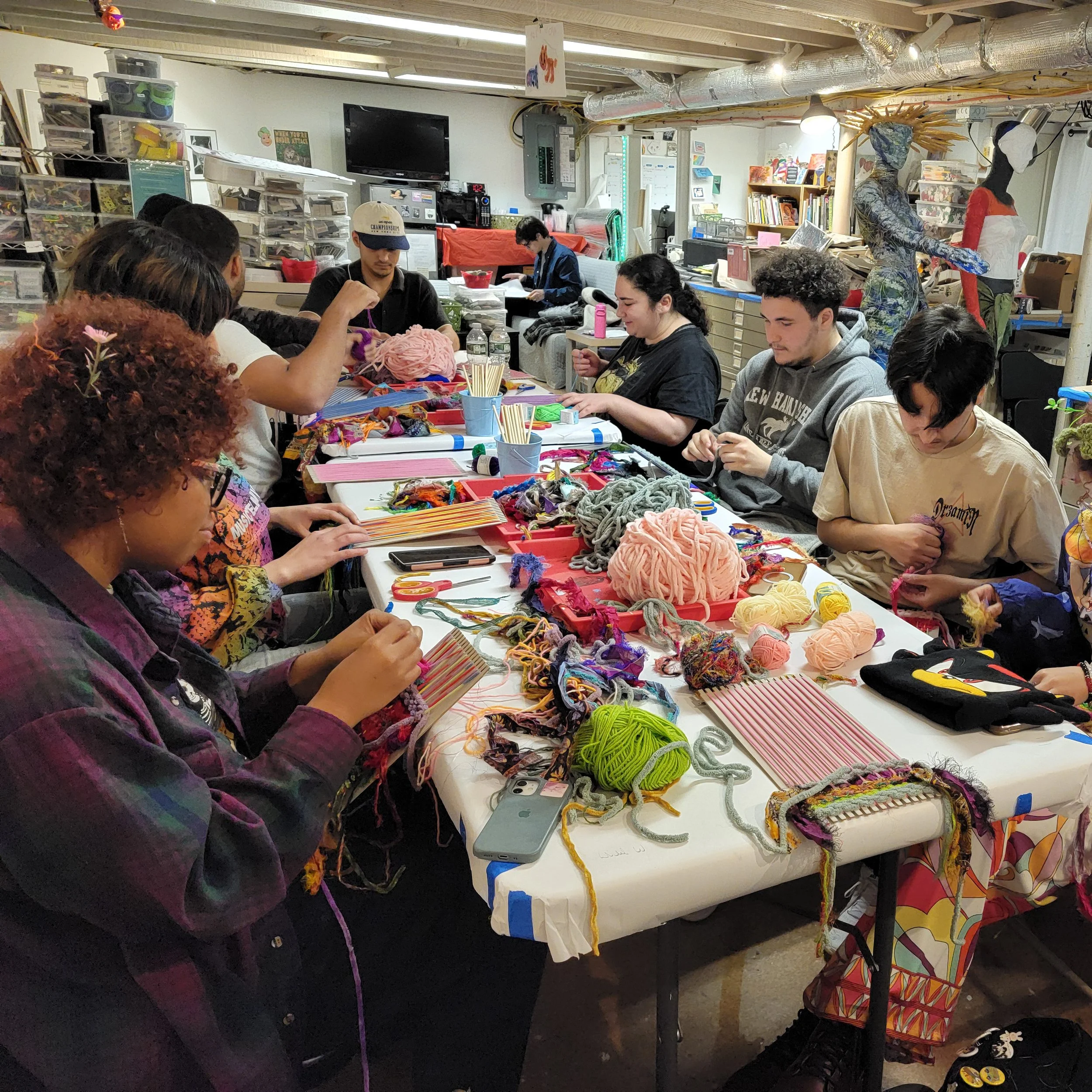 group of adutls around a table weaving yarn