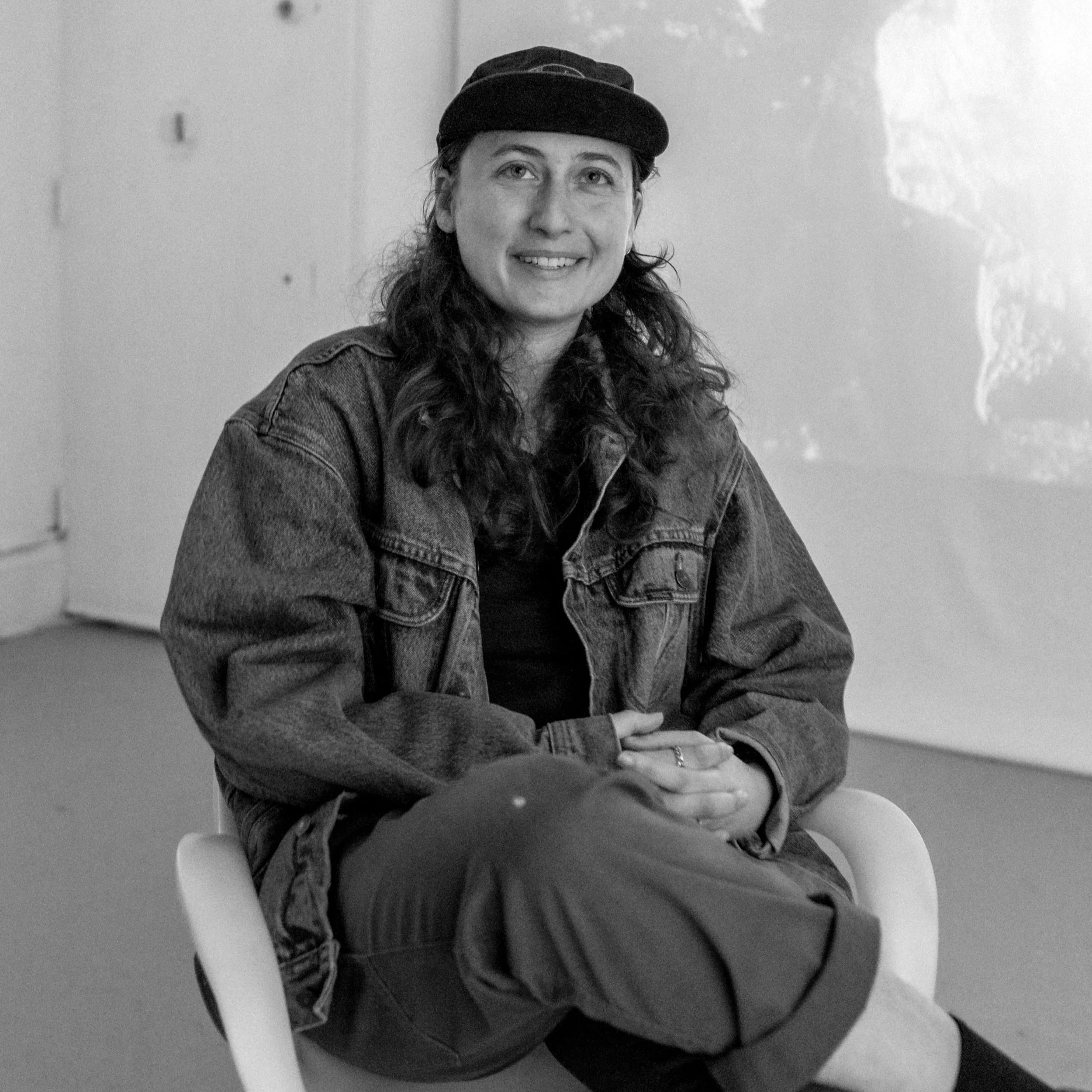 headshot of a person smiling, sitting on a chair in black and white
