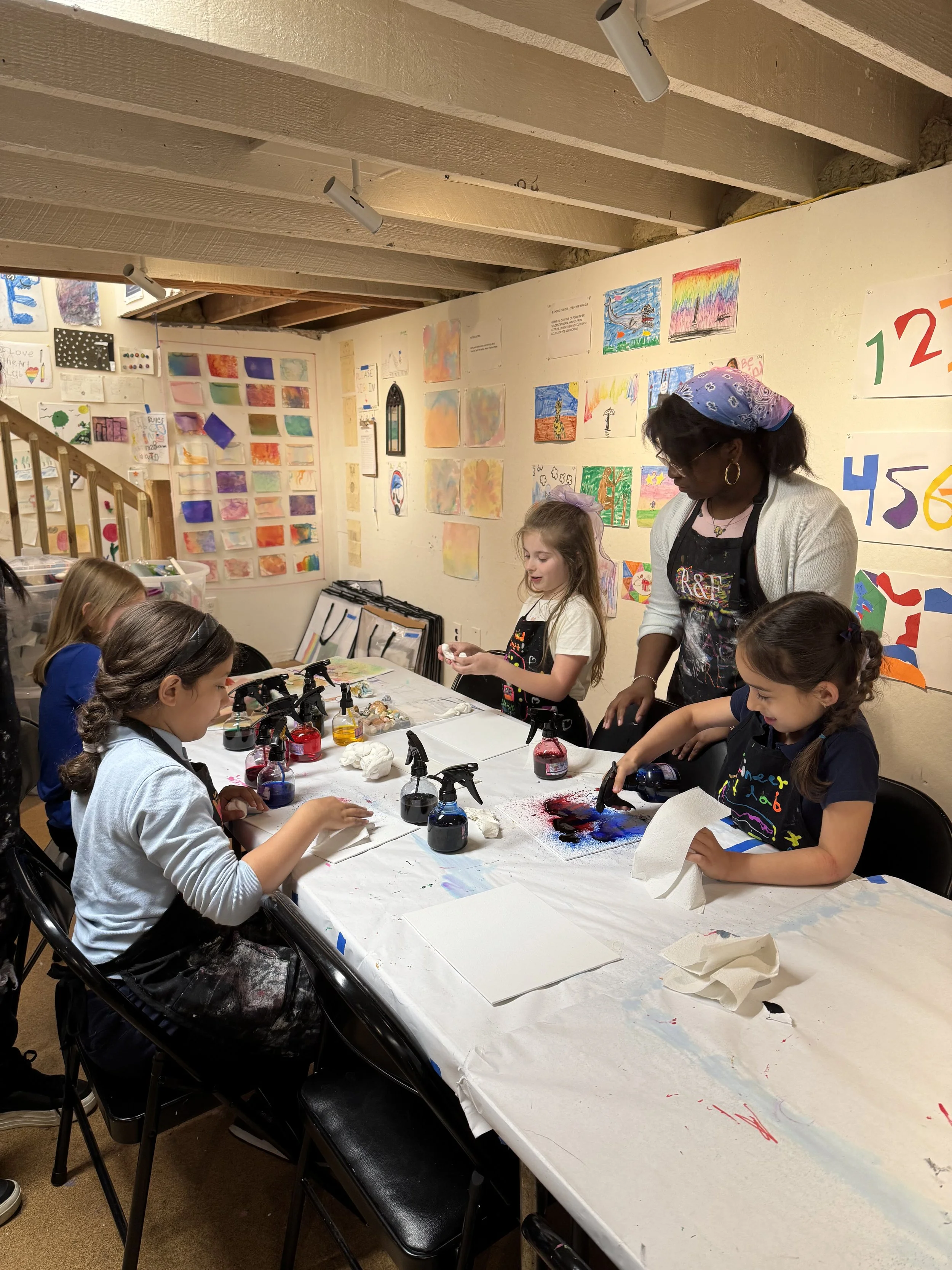 young students sitting around a table working with watercolors, led by a student teacher