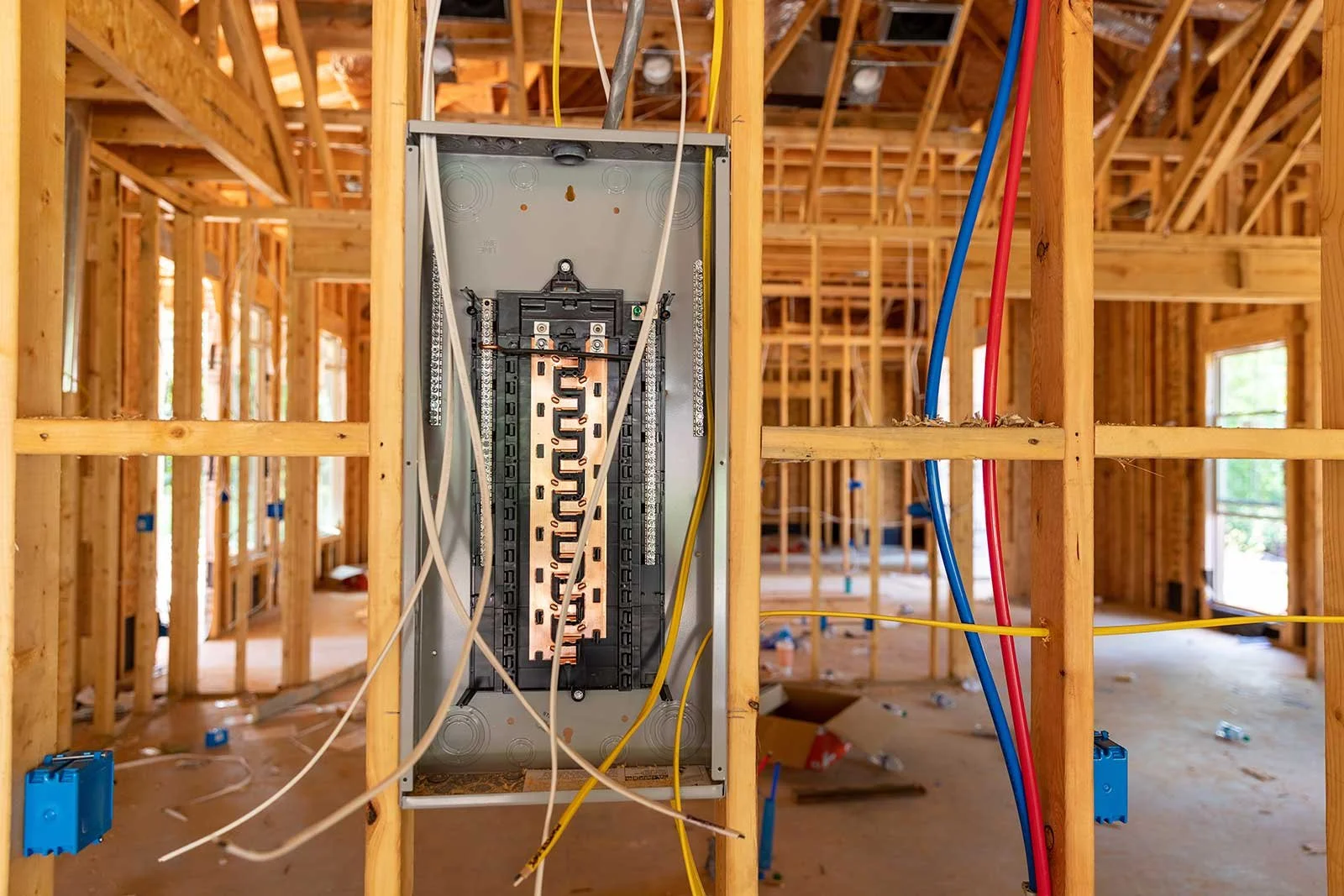 Electrical wiring and a circuit breaker panel inside a wooden house frame under construction.