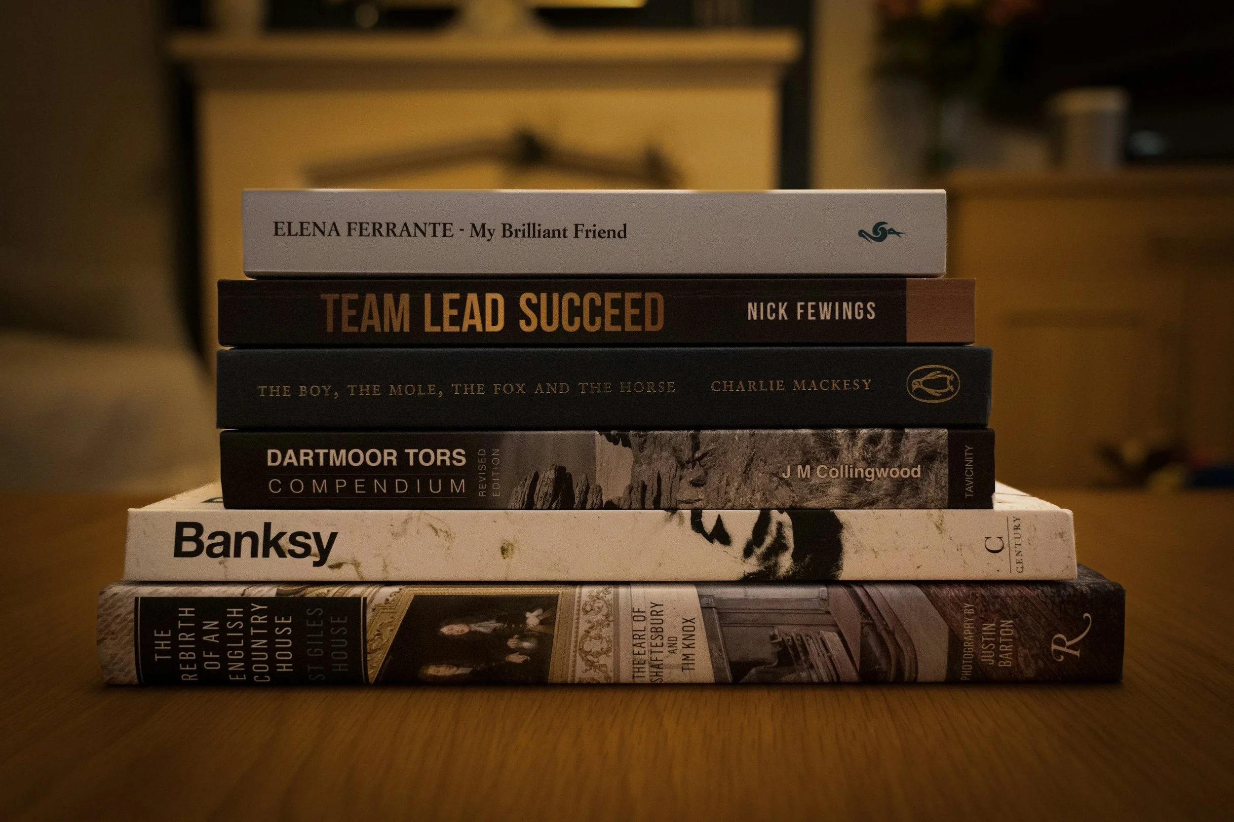 Stack of eight books on a wooden table with a blurred background.