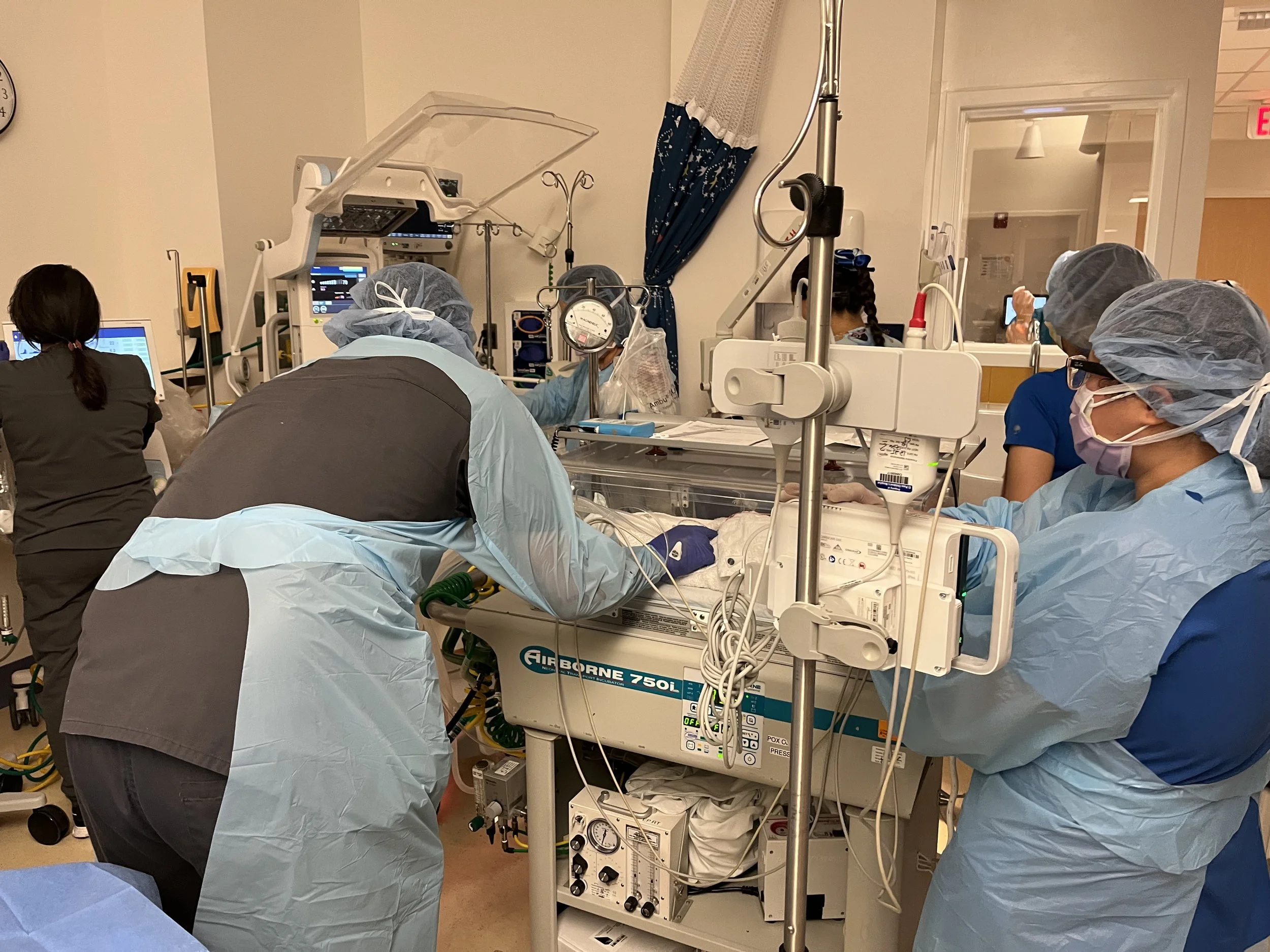 Medical team of healthcare professionals working in a hospital neonatal intensive care unit (NICU) with a newborn in an incubator, surrounded by medical equipment, monitors, and IV poles.