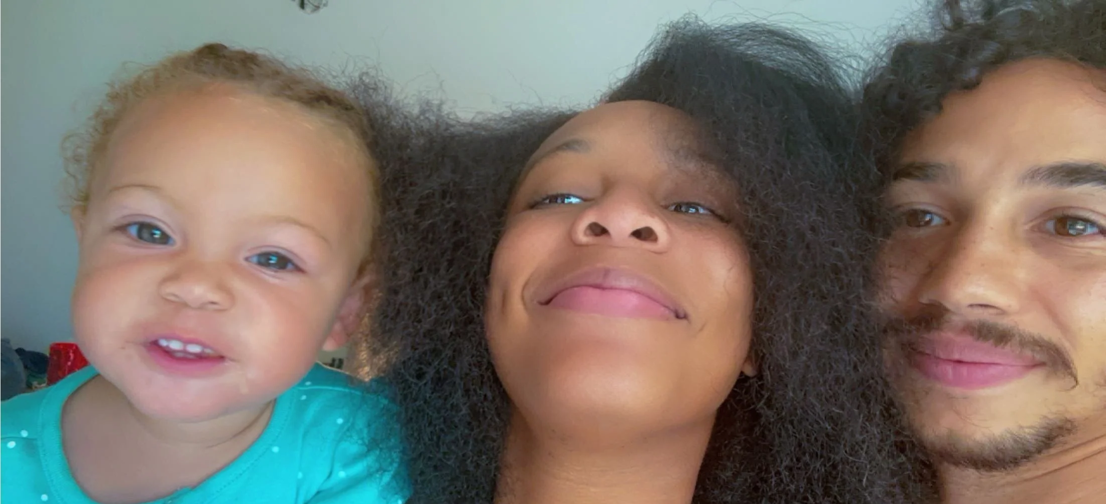 A close-up of three people lying down together, smiling at the camera.