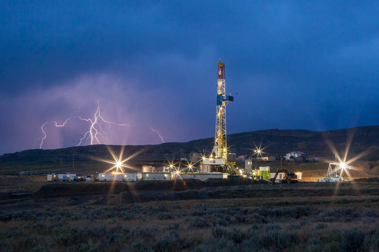 Lightning strikes just over the ridge from a drilling rig. Oil and gas industry marketing and communications photography.