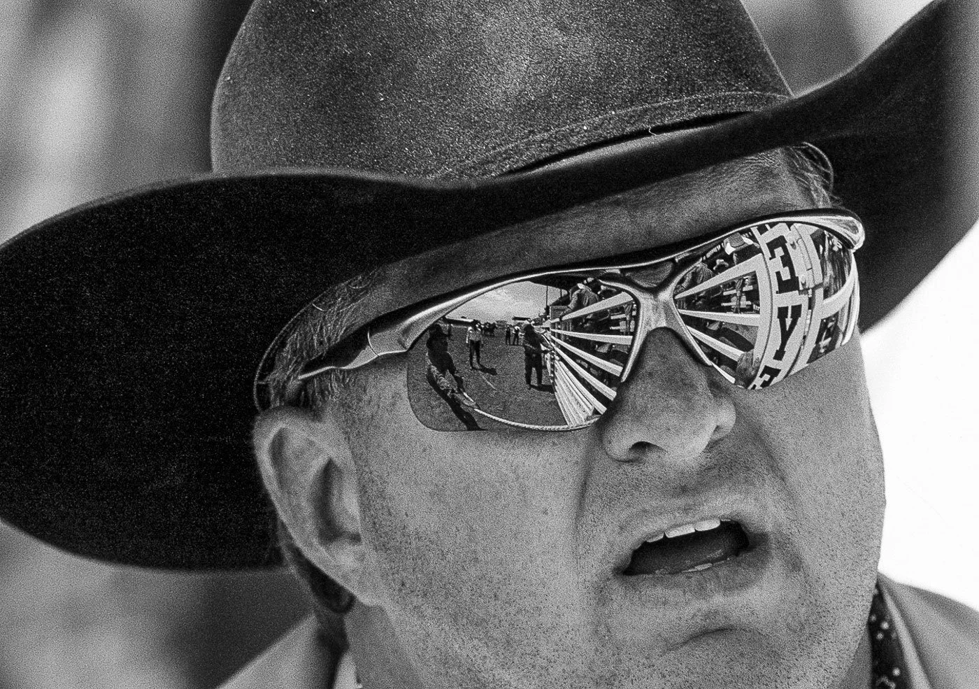 Rodeo photography, including detail and a black and white image. Cowboy with sunglasses and reflection in sunglasses opening a rough stock chute gate at Cheyenne Frontier Days.