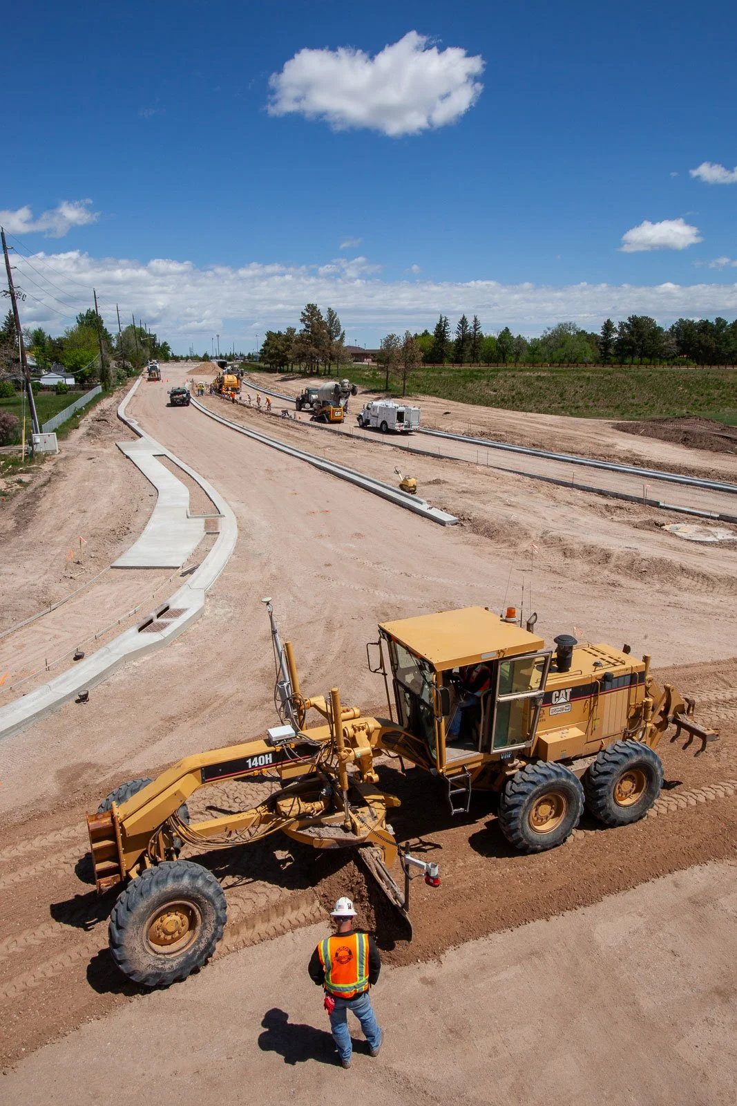 Road grader levels out dirt for a new road with construction workers watching.