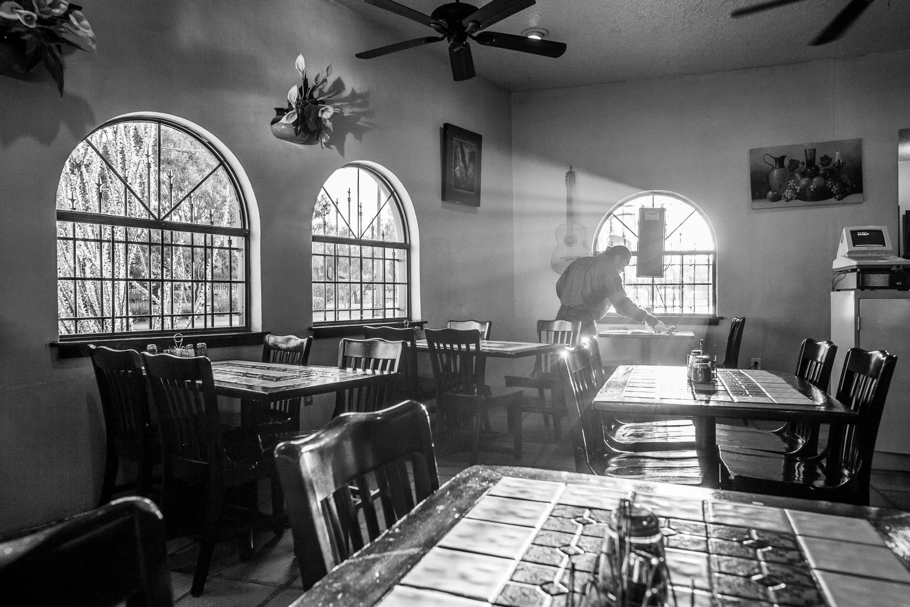 Black and white image at a Mexican restaurant in El Paso, Texas. Restaurant owner working with a beam of sunlight in the window.