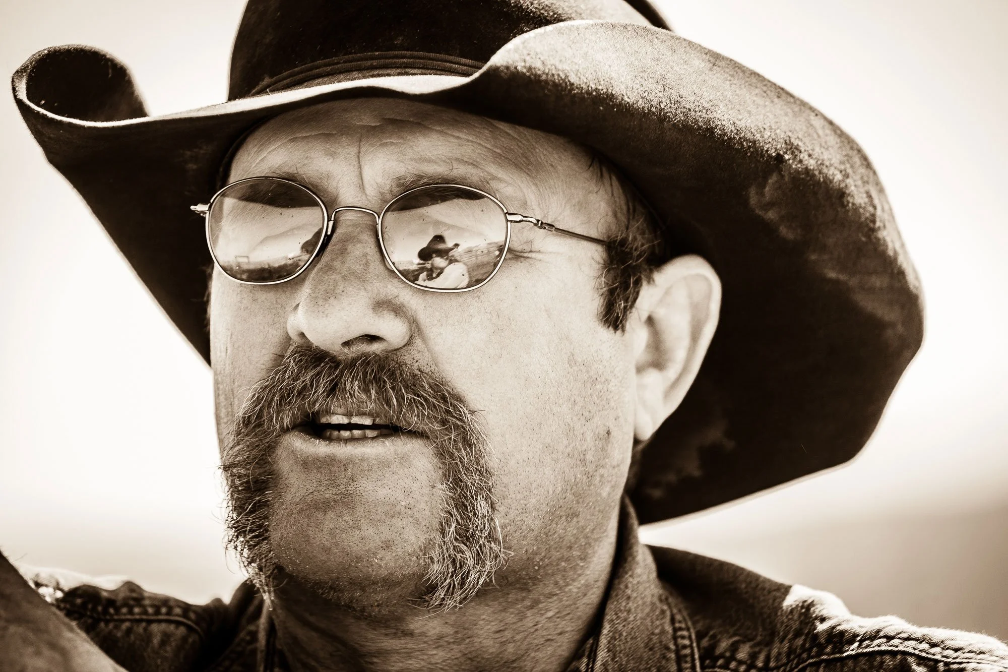 Cowboy's sunglasses reflecting a conversation with another cowboy at a branding at a ranch in Hawksprings, Wyoming.