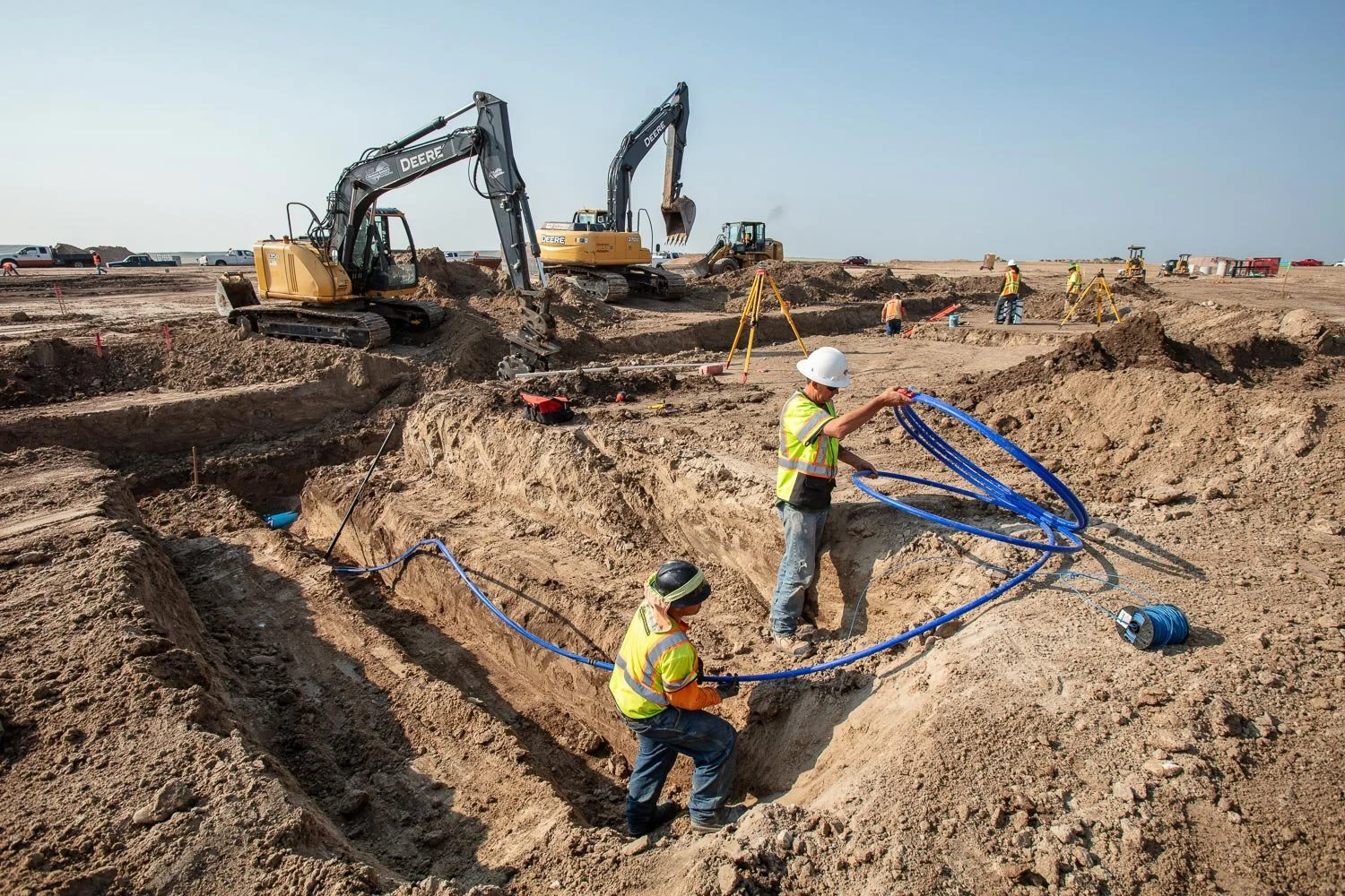 Construction workers work at a new subdivision with excavators in the background.